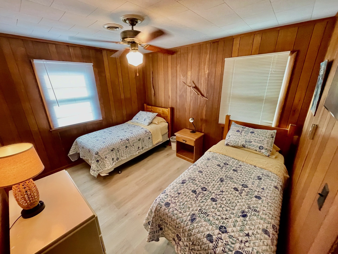 Relax in your cozy wood-paneled twin bedroom with comfy beds and coastal-themed linens, perfect for sharing with family or friends.