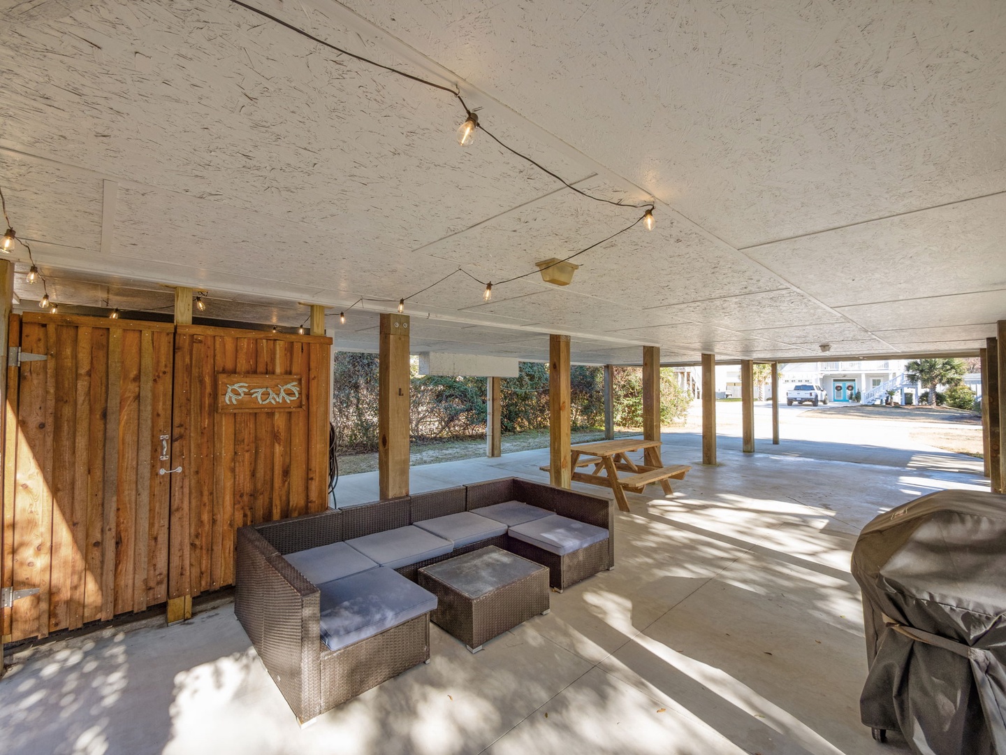 Relax in your covered outdoor lounge with cozy seating and twinkling lights overhead, perfect for unwinding after beach adventures.