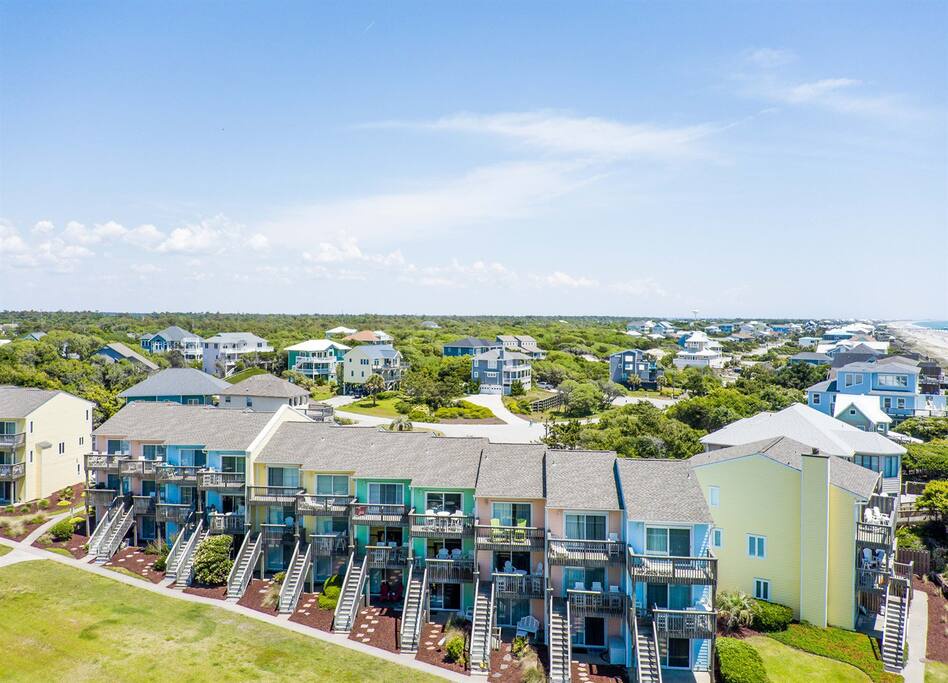 Colorful beach community with modern coastal homes scattered among lush greenery near the shoreline.