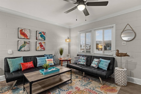 Relax in your stylish living space with comfortable leather seating, vibrant artwork, and a cooling ceiling fan overhead.