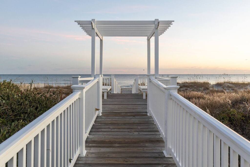 A charming beachfront boardwalk leads to pristine sandy shores, featuring a shaded pavilion perfect for watching spectacular sunsets over the ocean.