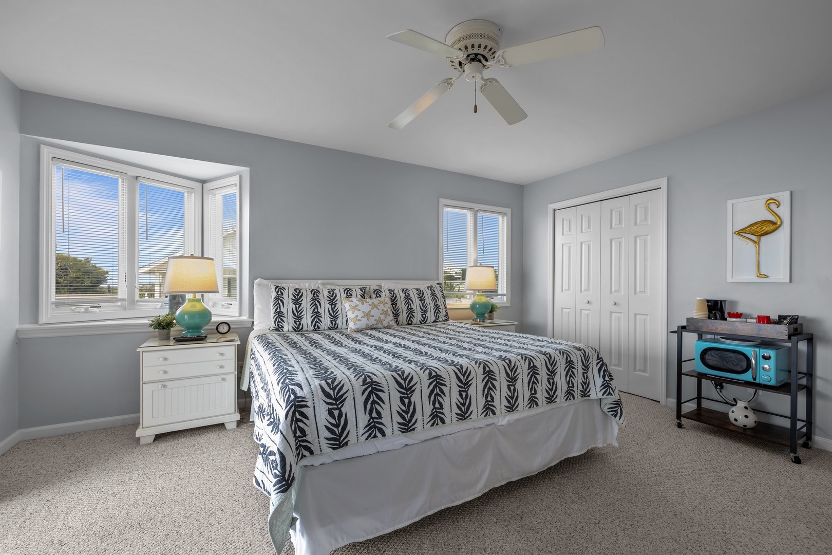 Your spacious bedroom features coastal charm with soft gray walls, stylish leaf-pattern bedding, and a gentle ceiling fan for comfort.