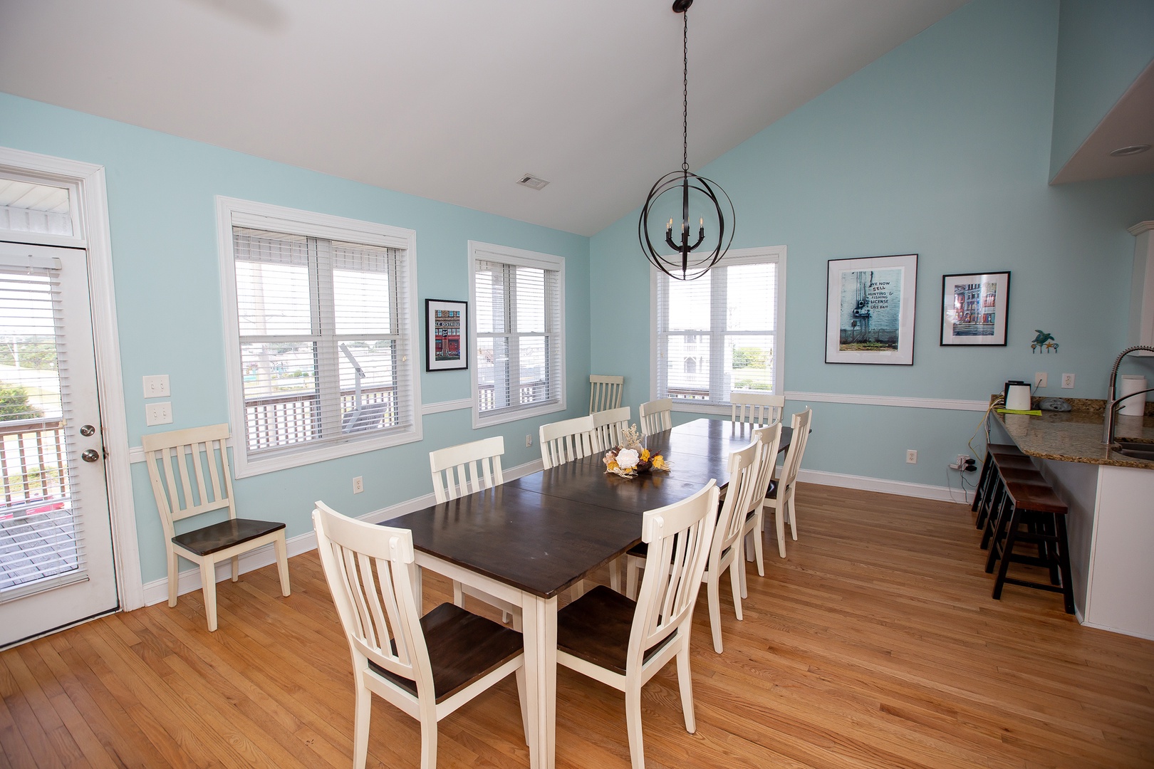 Gather your family around this spacious dining table in the bright, airy room with coastal blue walls and natural light streaming through multiple windows.