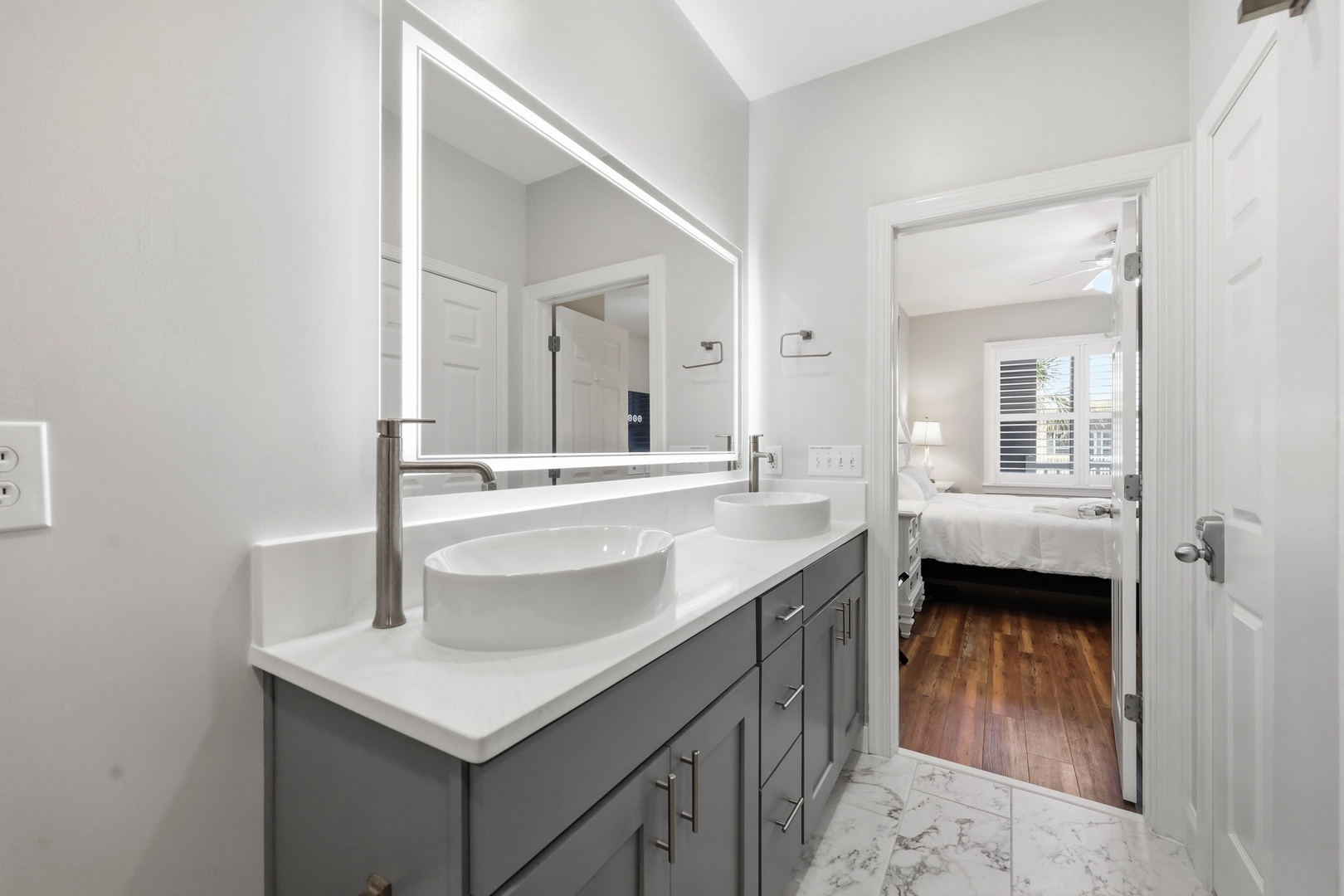 Step into your spa-like ensuite bathroom with dual vessel sinks, LED-lit mirror, and elegant marble-look tile connecting to your serene bedroom retreat.