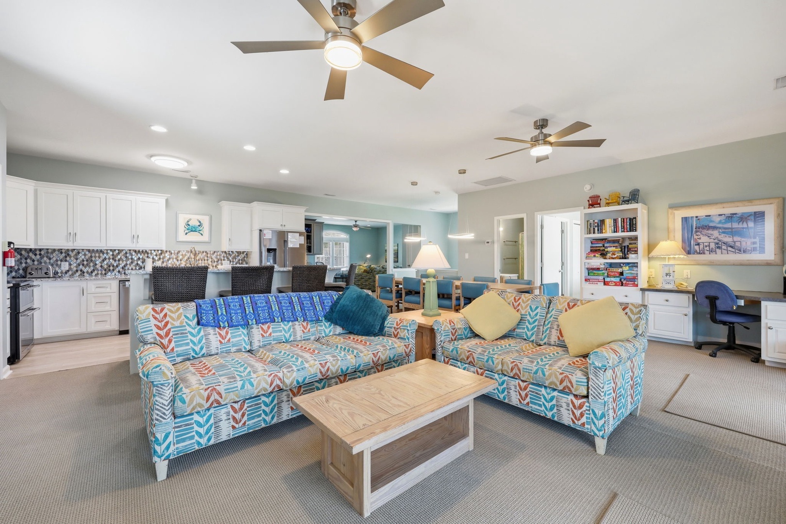 Settle into your bright open-plan retreat where vibrant coastal-themed sofas invite relaxation, the kitchen awaits your culinary creations, and ceiling fans keep every corner refreshingly cool.