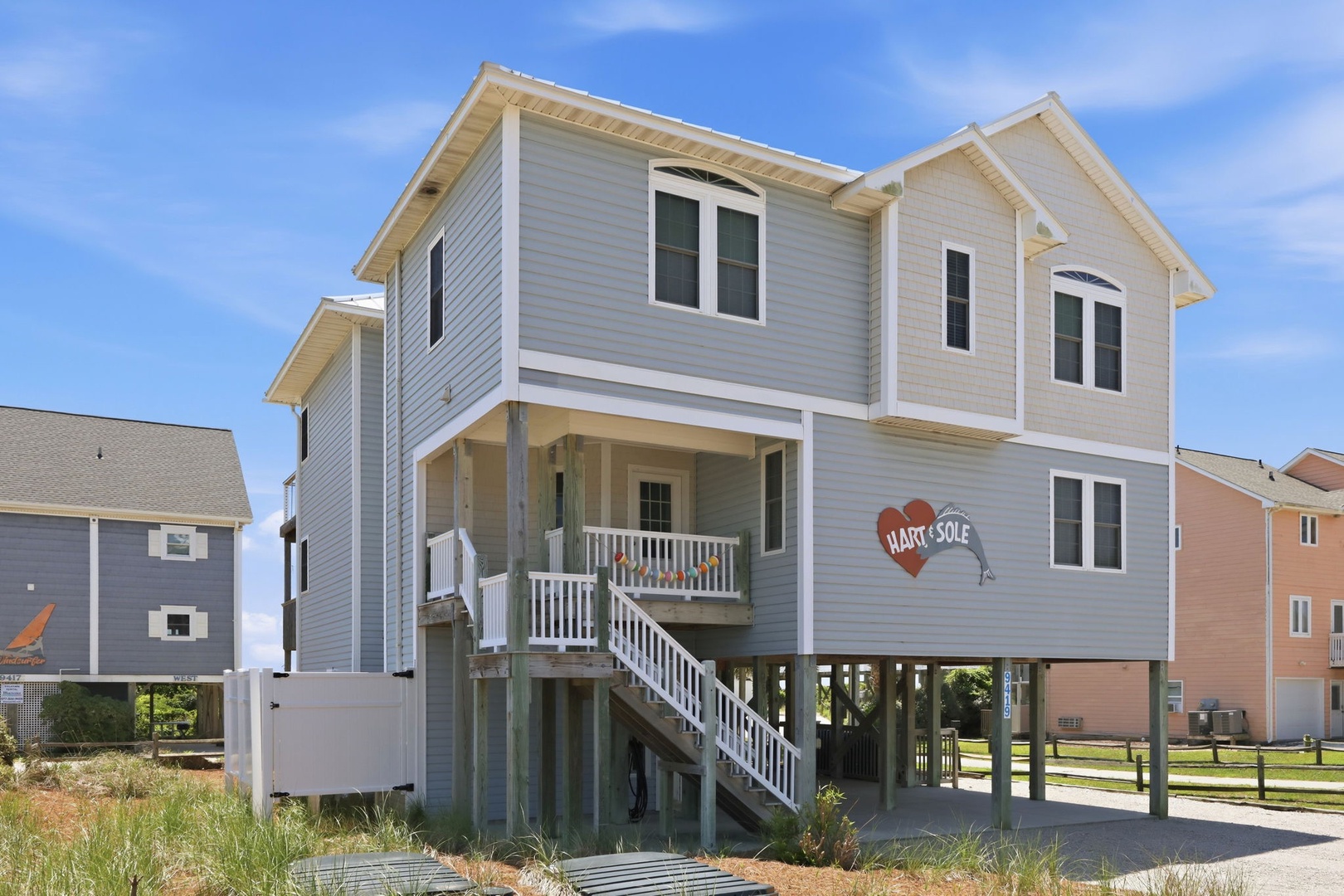 A charming coastal property elevated on stilts with a welcoming heart-shaped sign, located in a peaceful waterfront neighborhood with convenient access to the shore.