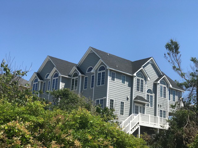 Spacious coastal property with traditional architecture set among mature landscaping under clear blue skies.
