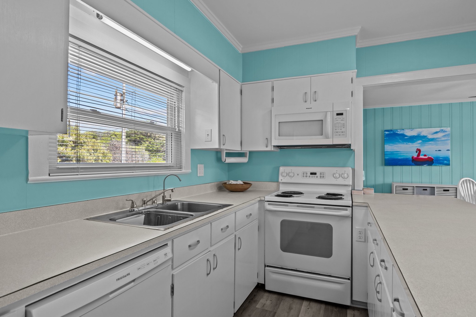 Your bright kitchen features cheerful turquoise walls and full appliances for home-cooked meals with natural light streaming through blinds.