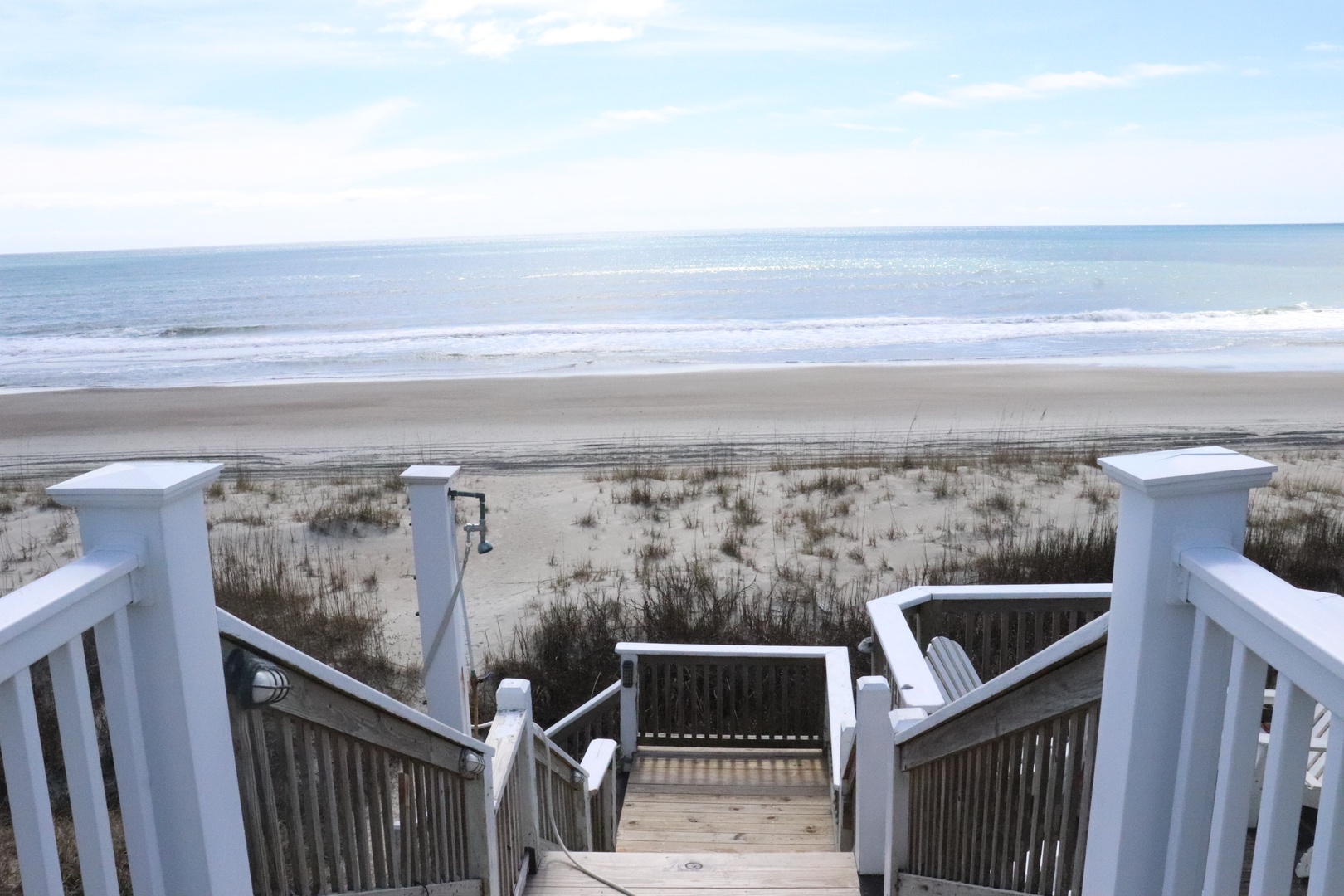 Wooden walkway leads to pristine sandy beach with ocean waves and coastal dunes.
