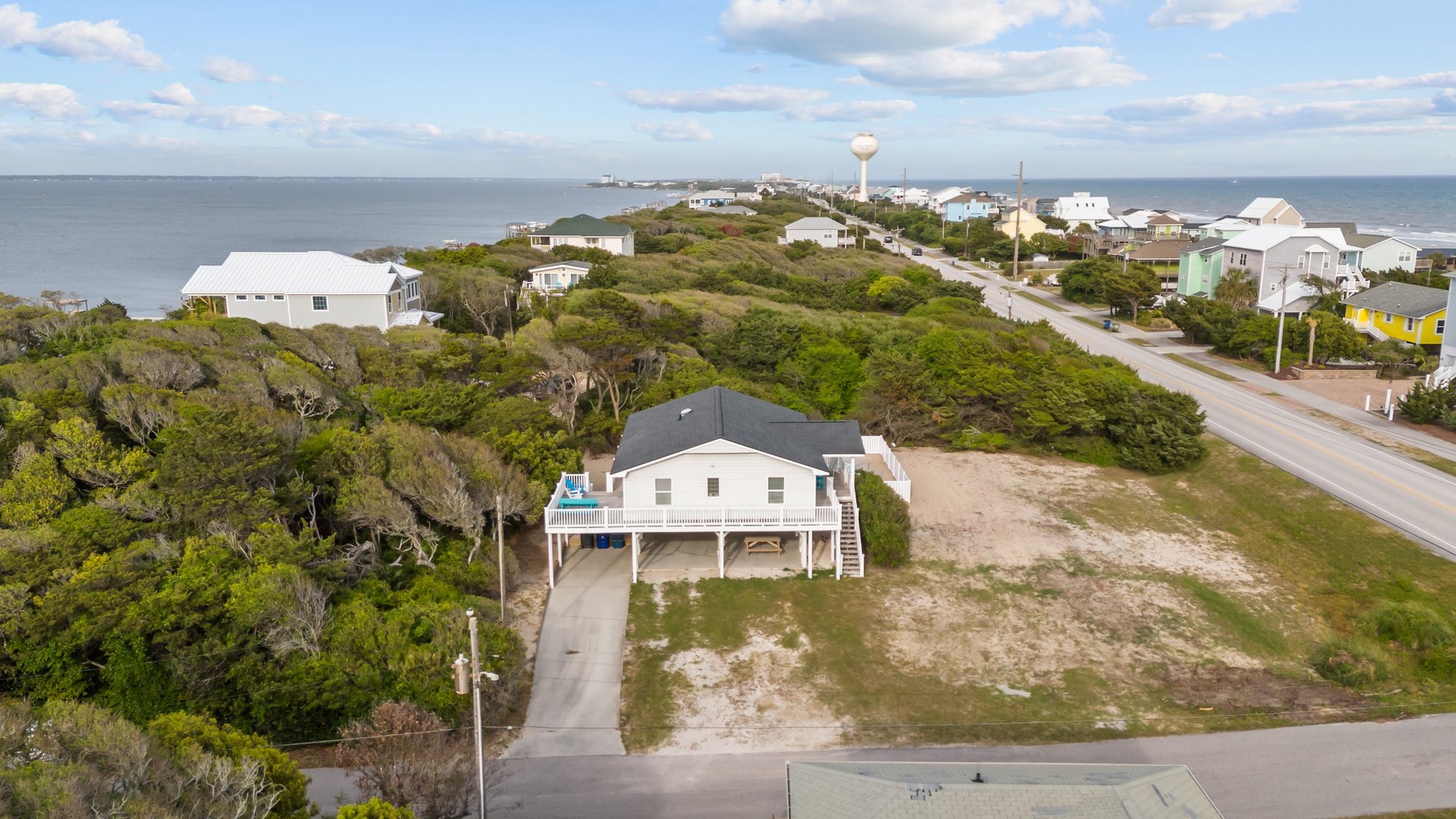 Aerial view of coastal property surrounded by lush vegetation and neighboring beach homes near the shoreline.