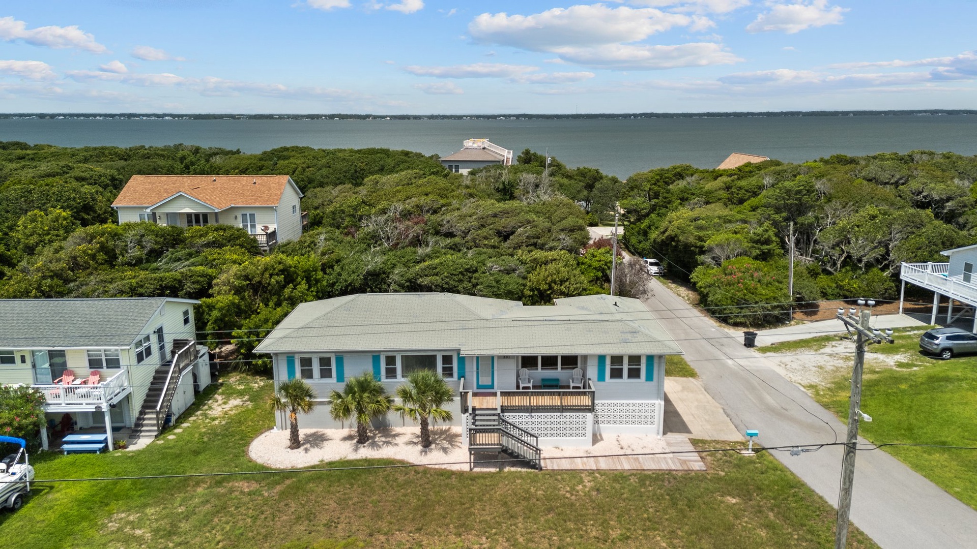 Coastal retreat nestled among mature trees just steps from the water, featuring elevated deck and tropical landscaping in peaceful neighborhood setting.