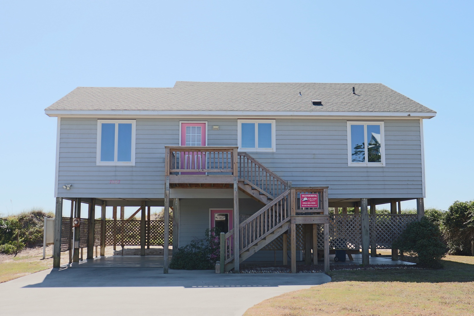 Coastal vacation home on stilts with covered parking and staircase entrance, perfect beach retreat setting.