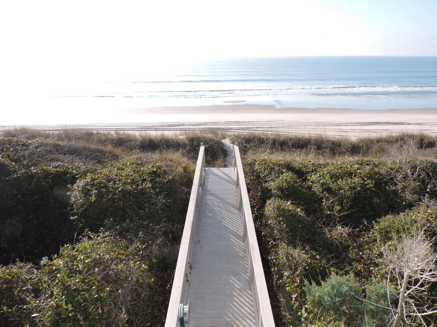 Private beach access walkway leads through coastal dunes to pristine sandy shoreline with gentle waves.
