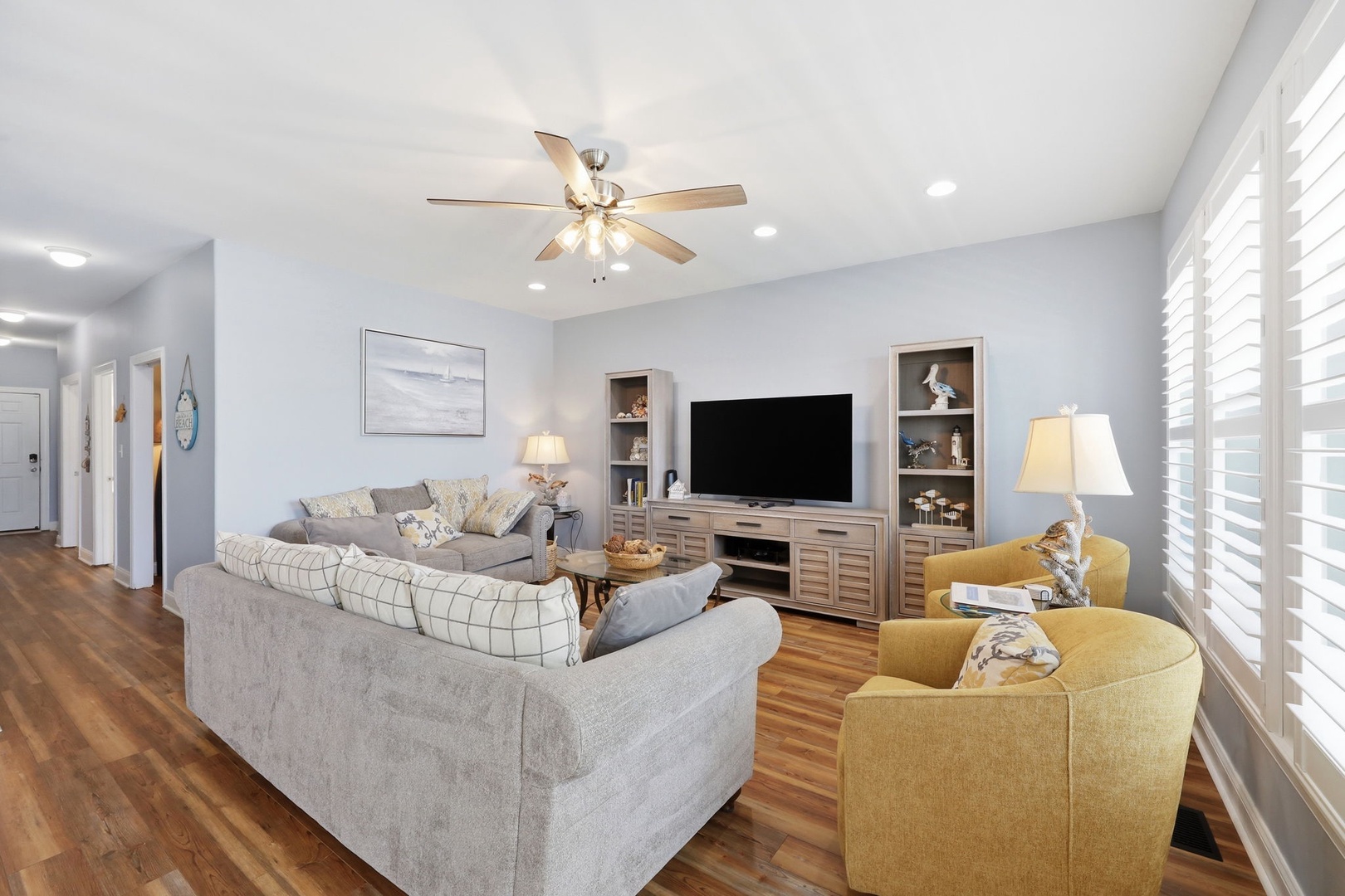 Settle into your bright, inviting living room where warm wood floors and a cozy sectional await. Sunlight filters through plantation shutters while you enjoy your favorite shows.