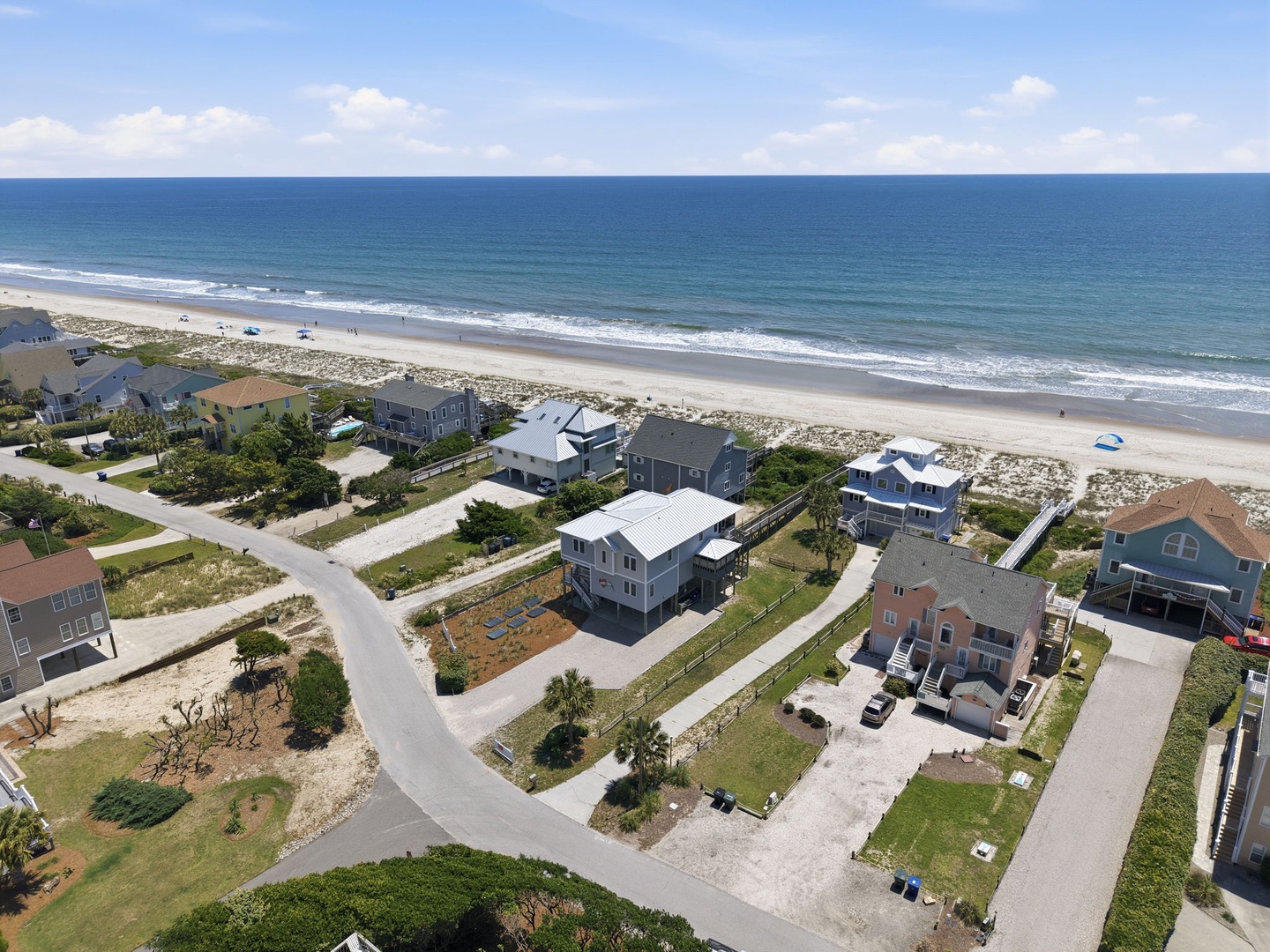 Aerial view of beachfront vacation homes along a pristine sandy shore, showcasing the coastal neighborhood and easy beach access.