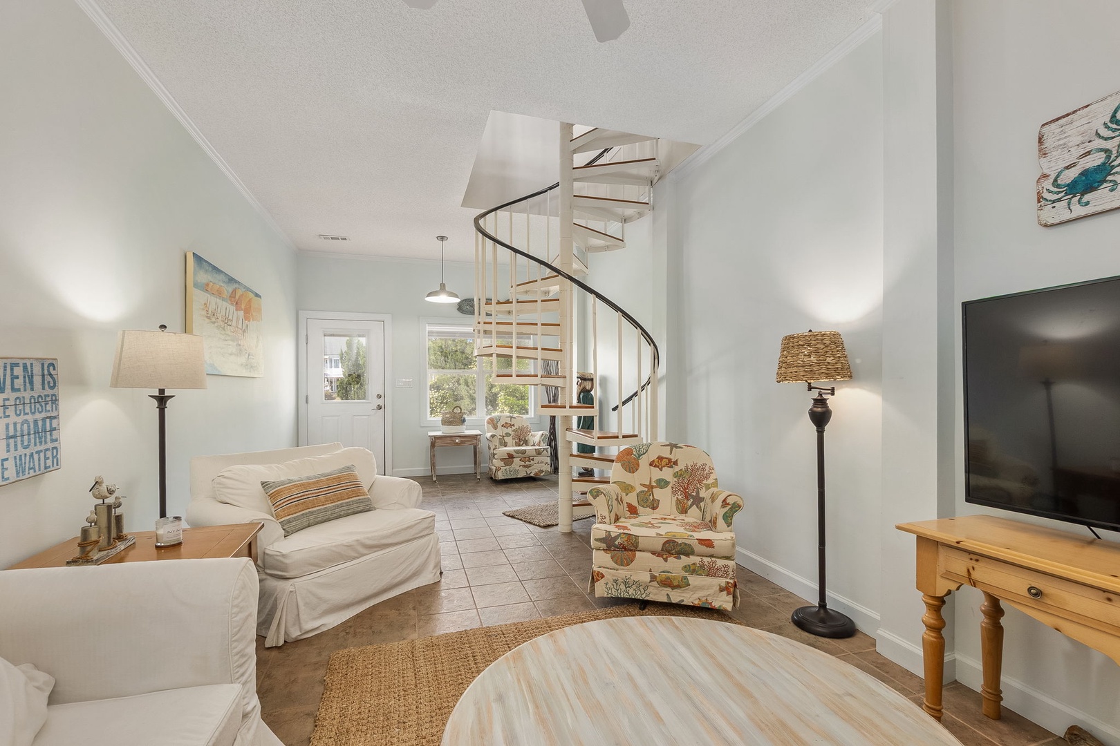 Relax in your bright, airy living space featuring charming coastal decor, comfortable seating, and a unique spiral staircase leading to your loft.