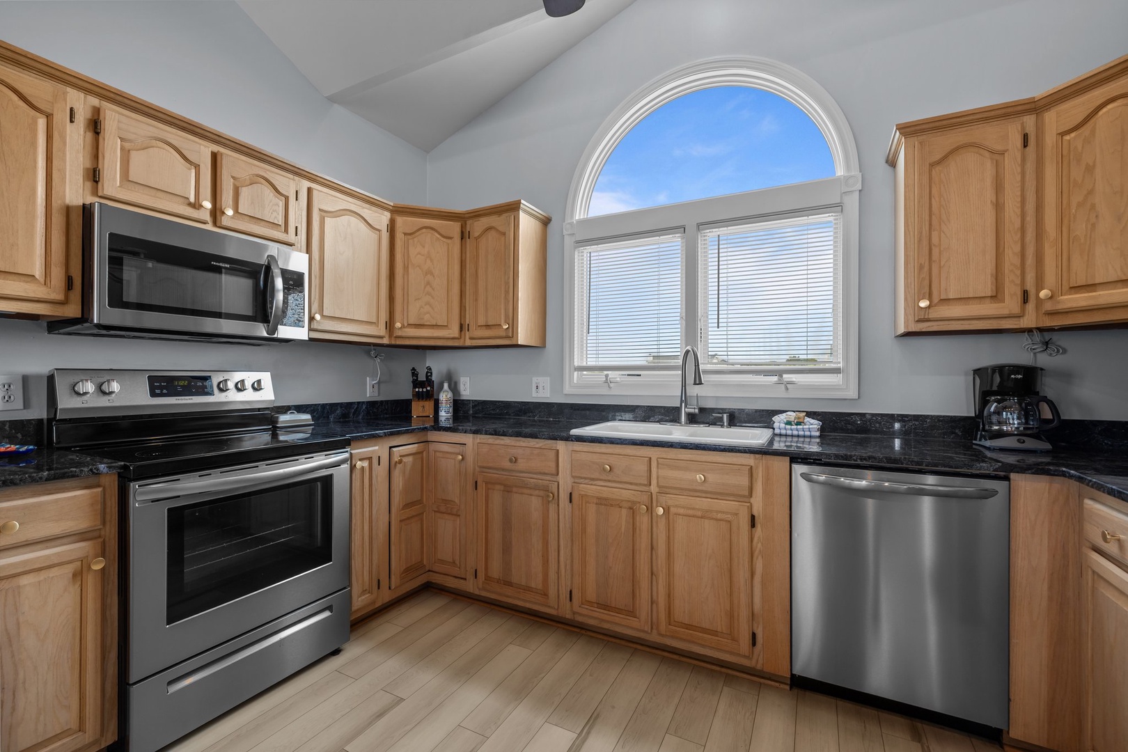 Your fully equipped kitchen features granite counters, stainless steel appliances, and abundant cabinet space beneath a bright arched window.