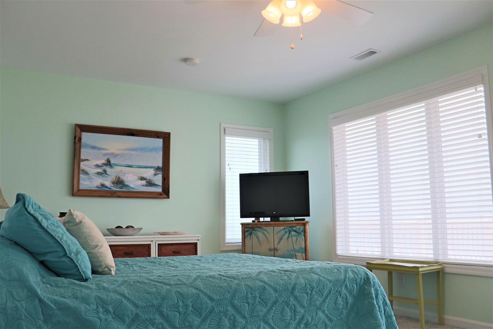 Rest peacefully in this coastal-themed bedroom featuring soft mint walls, ocean artwork, and your own flat-screen TV for cozy evenings.
