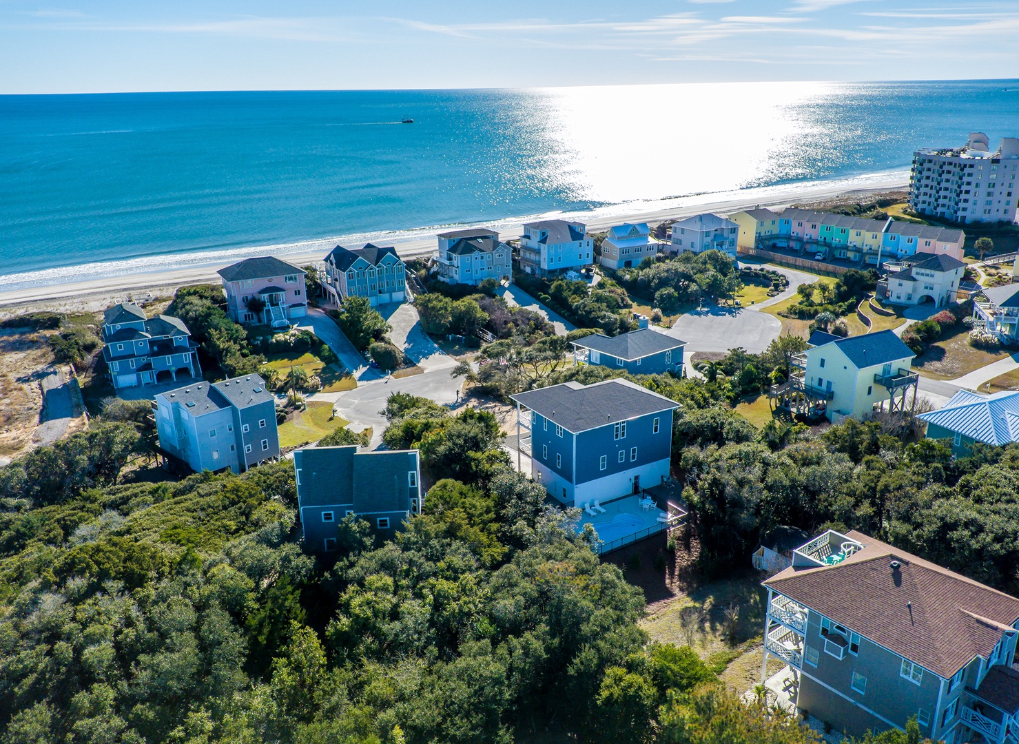 Charming beachfront community with colorful vacation homes nestled among coastal trees, offering direct access to pristine sandy shores and sparkling ocean waters.