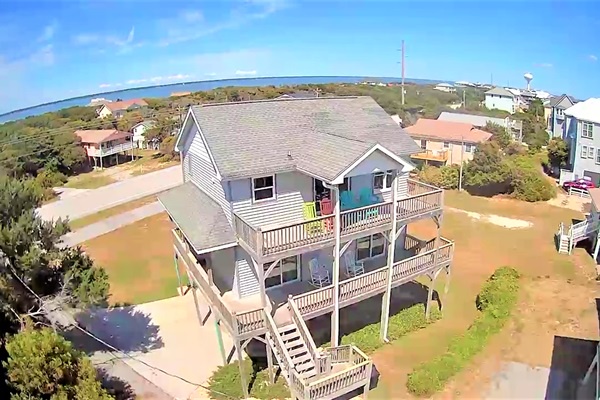 Elevated coastal retreat with multi-level decks overlooking a serene beach community and ocean beyond.