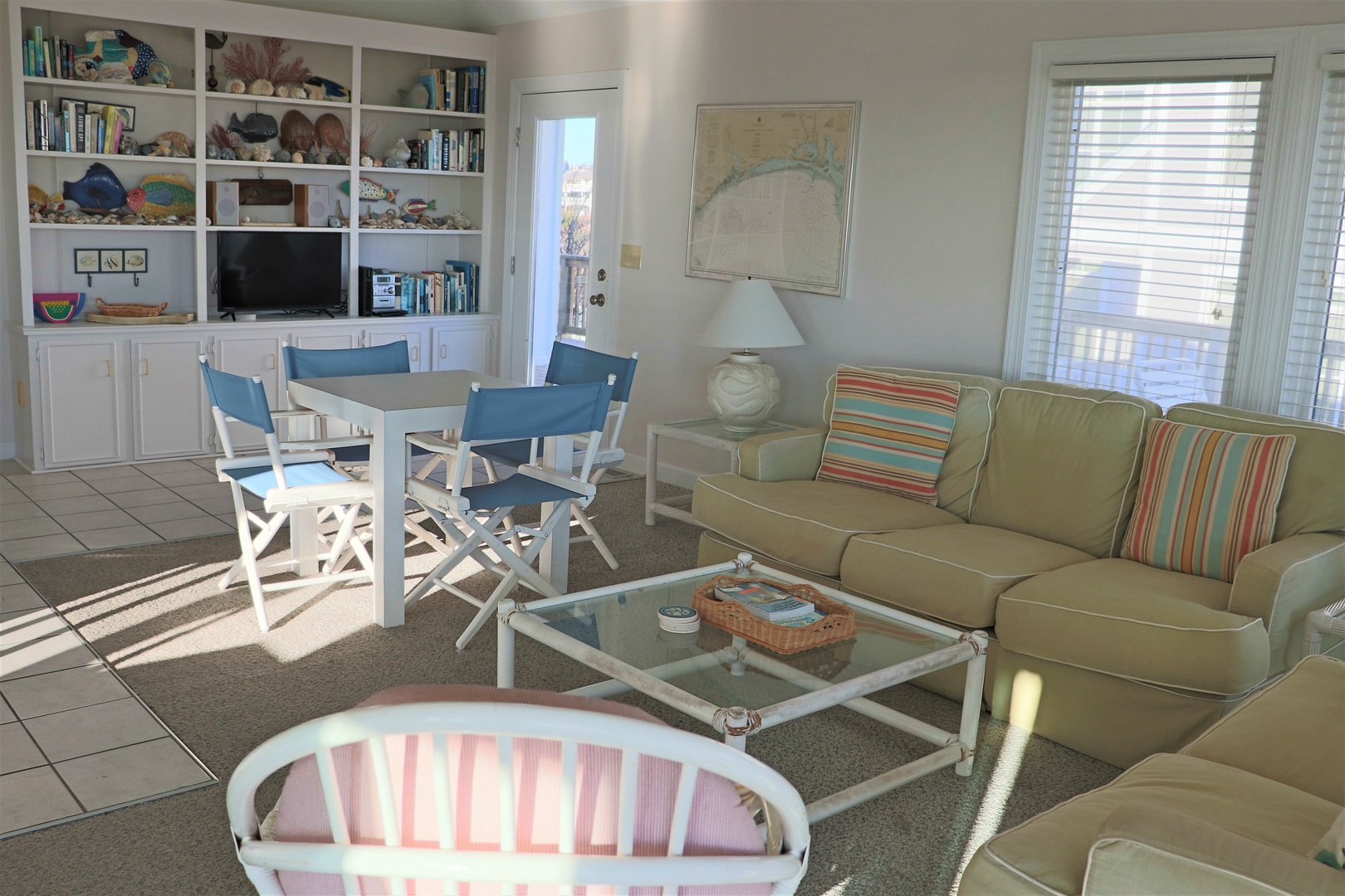 Settle into your bright coastal living room where warm sunlight filters through blinds, highlighting the sectional sofa and cheerful nautical decor.