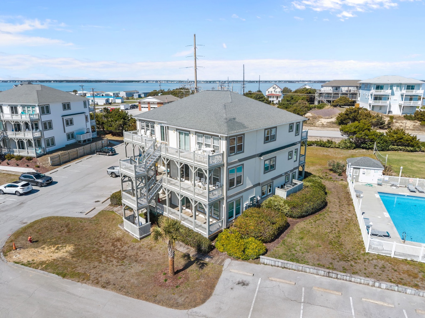 Coastal vacation rental with multiple balconies overlooks the ocean, surrounded by community pool and waterfront views.