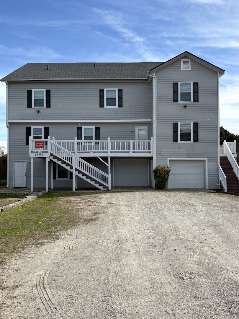 Modern gray building with multiple levels and white trim sits on sandy beachfront grounds.