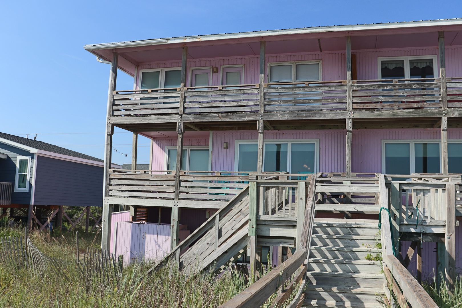 A charming pink beach house elevated on stilts with wooden walkways and multiple balconies under clear blue skies.
