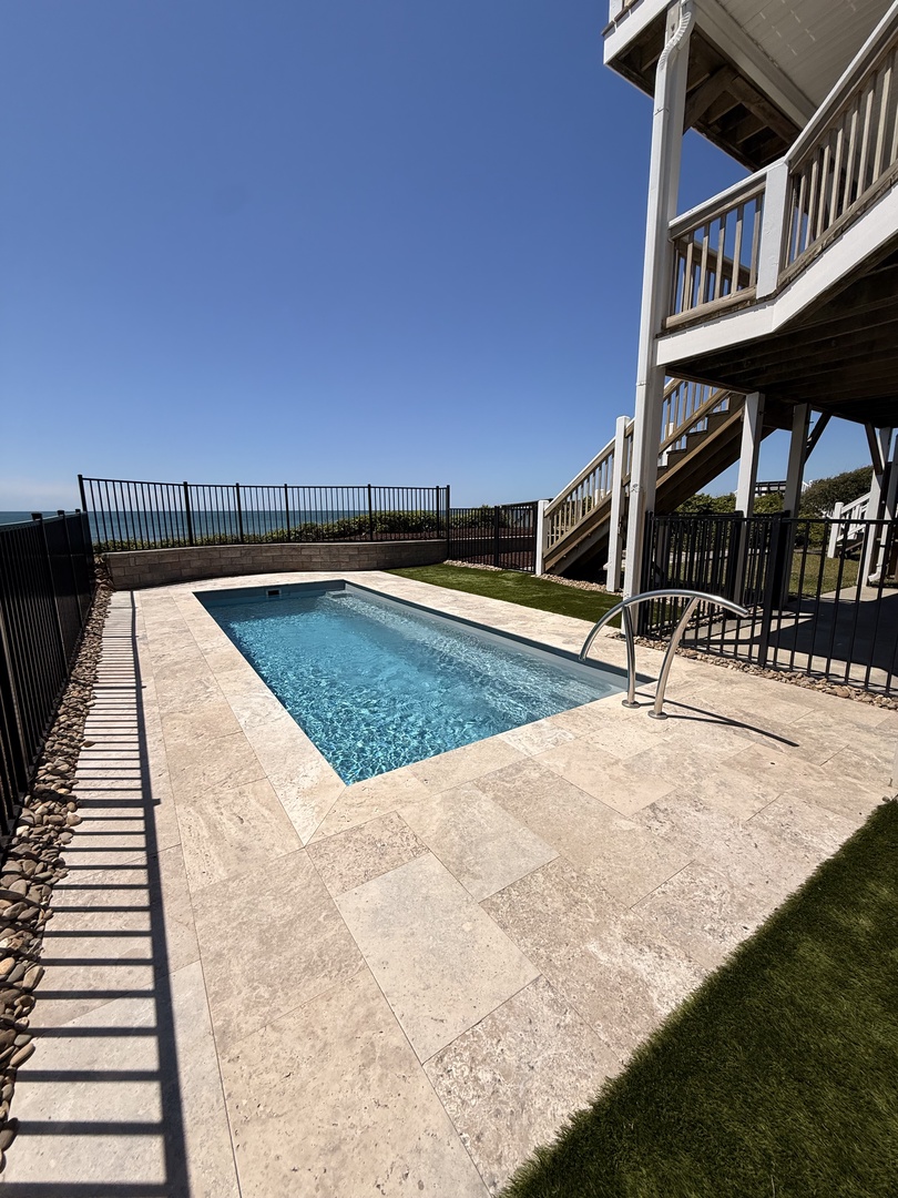 Modern architectural design frames a sparkling pool surrounded by travertine stone, with sleek slatted balconies and lush lawn nearby—a stylish setting for relaxation.