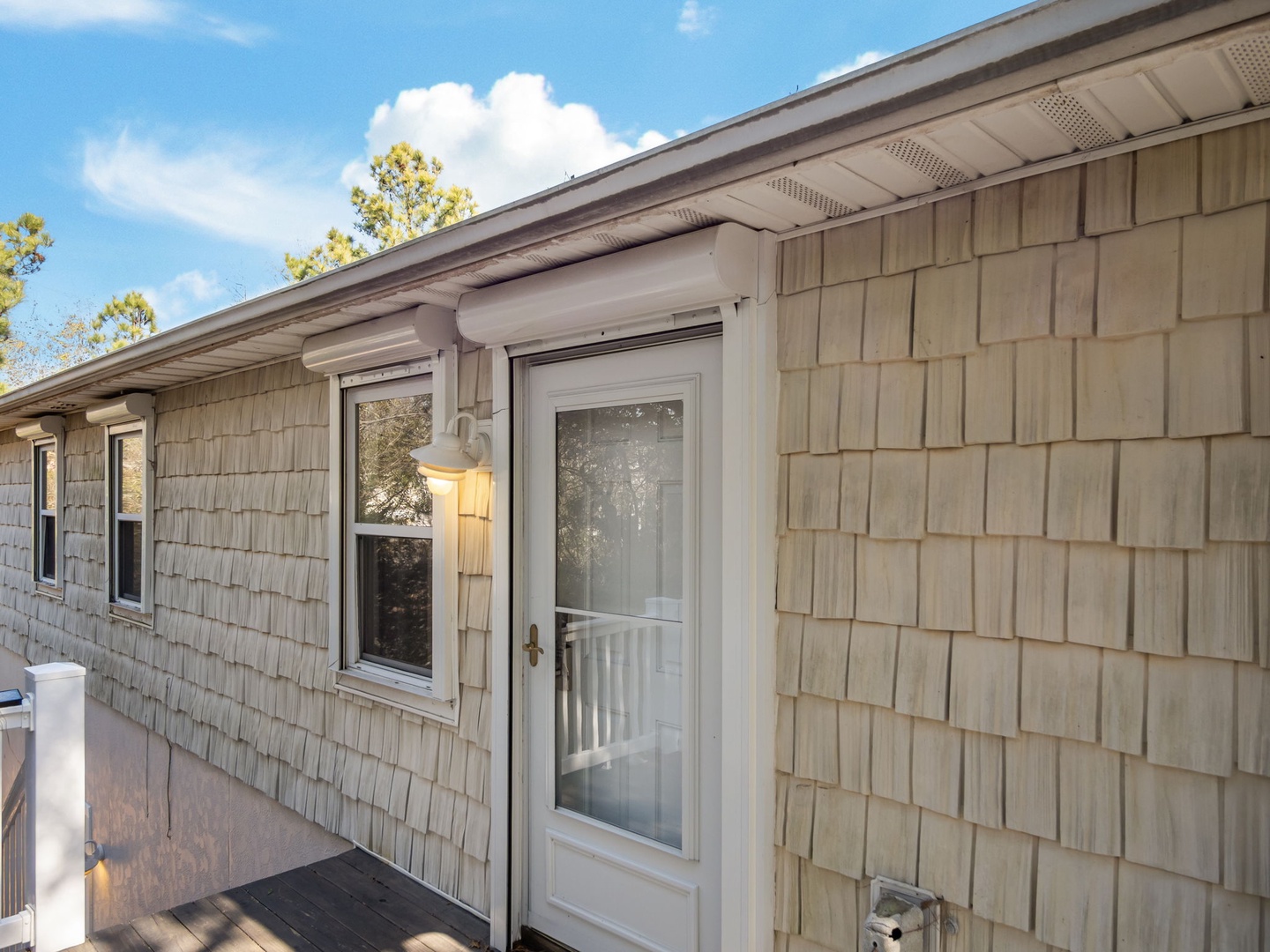 Charming coastal-style property with cedar shingle siding and welcoming entrance under bright blue skies.