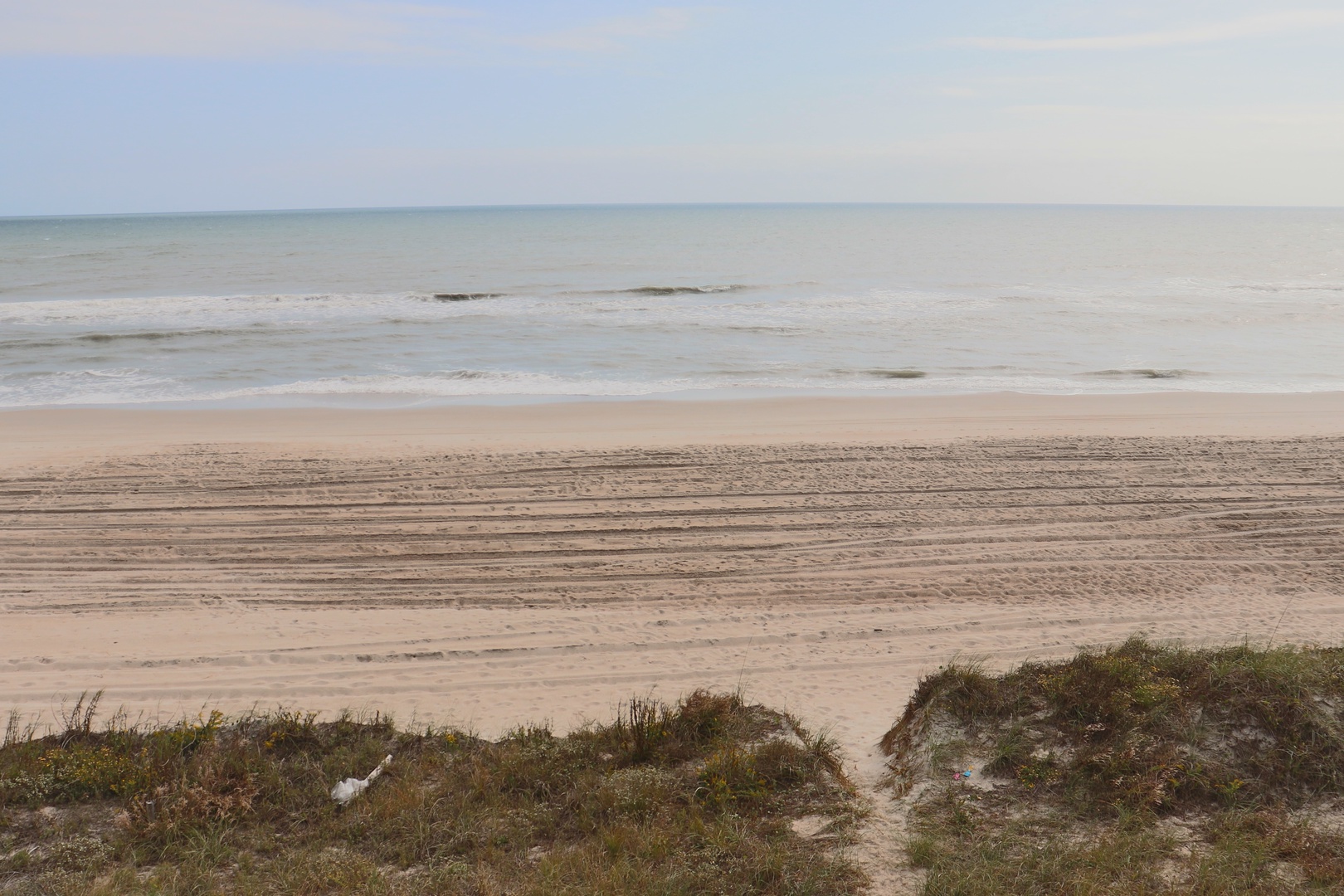 Pristine sandy beach stretches along the coastline with gentle waves and natural dune vegetation in the foreground.