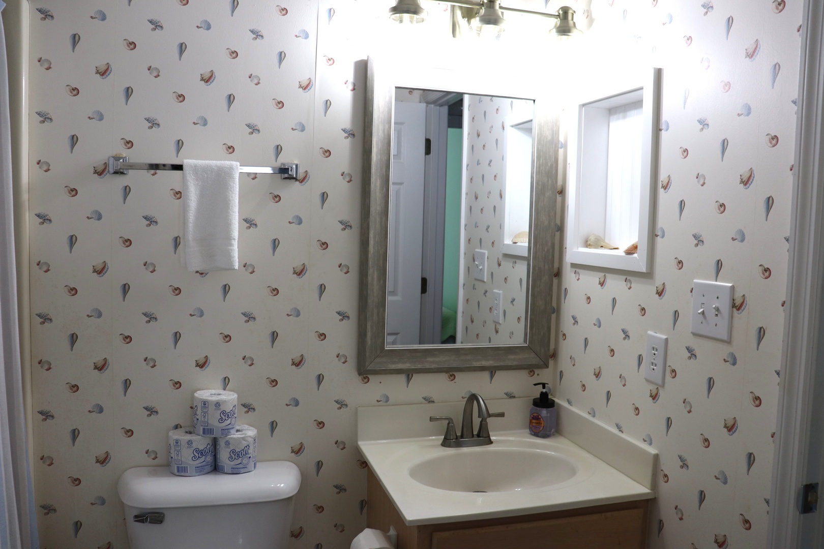 Your charming powder room features whimsical seashell wallpaper and thoughtful amenities, creating a delightful coastal retreat for freshening up.