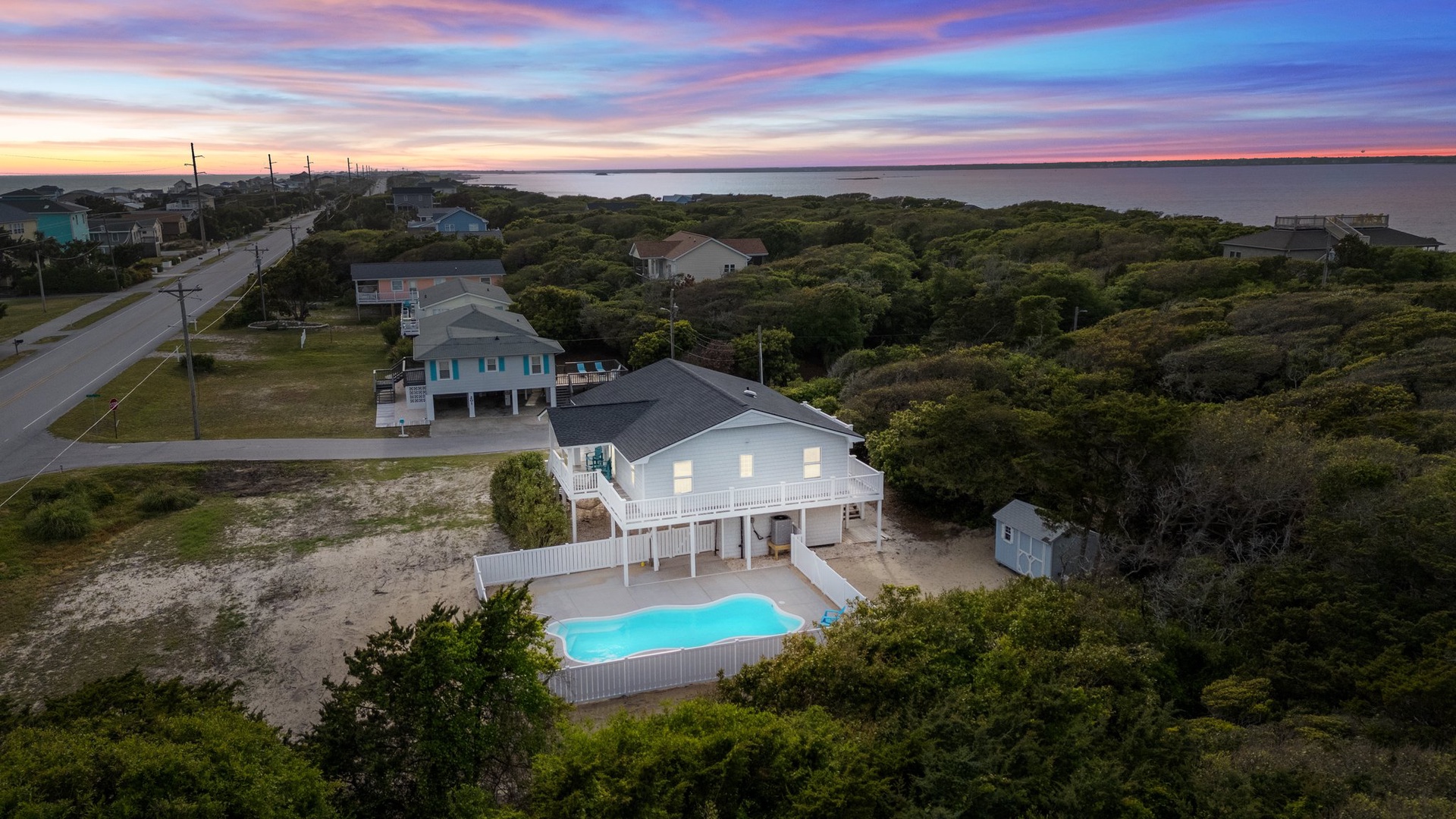 Coastal vacation home with private pool nestled among lush vegetation near the water's edge under dramatic evening skies.