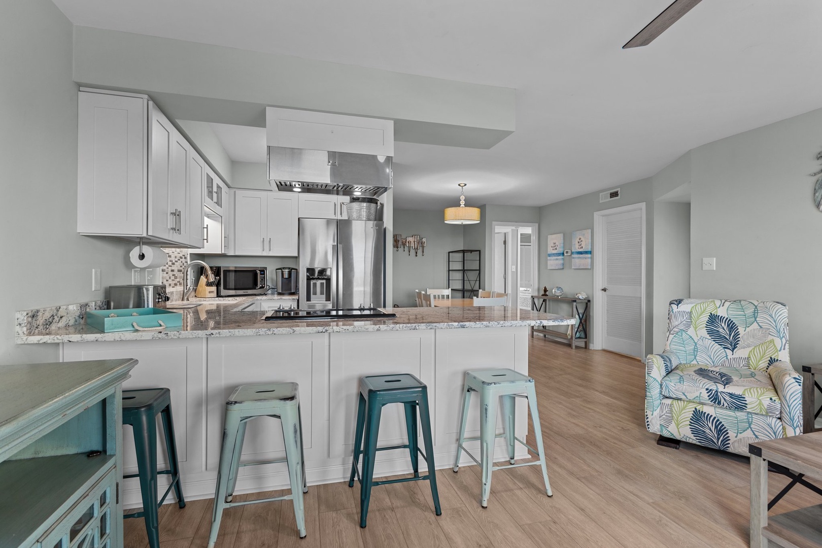 Your fully equipped kitchen features granite counters, stainless appliances, and cheerful turquoise stools perfect for morning coffee or meal prep.