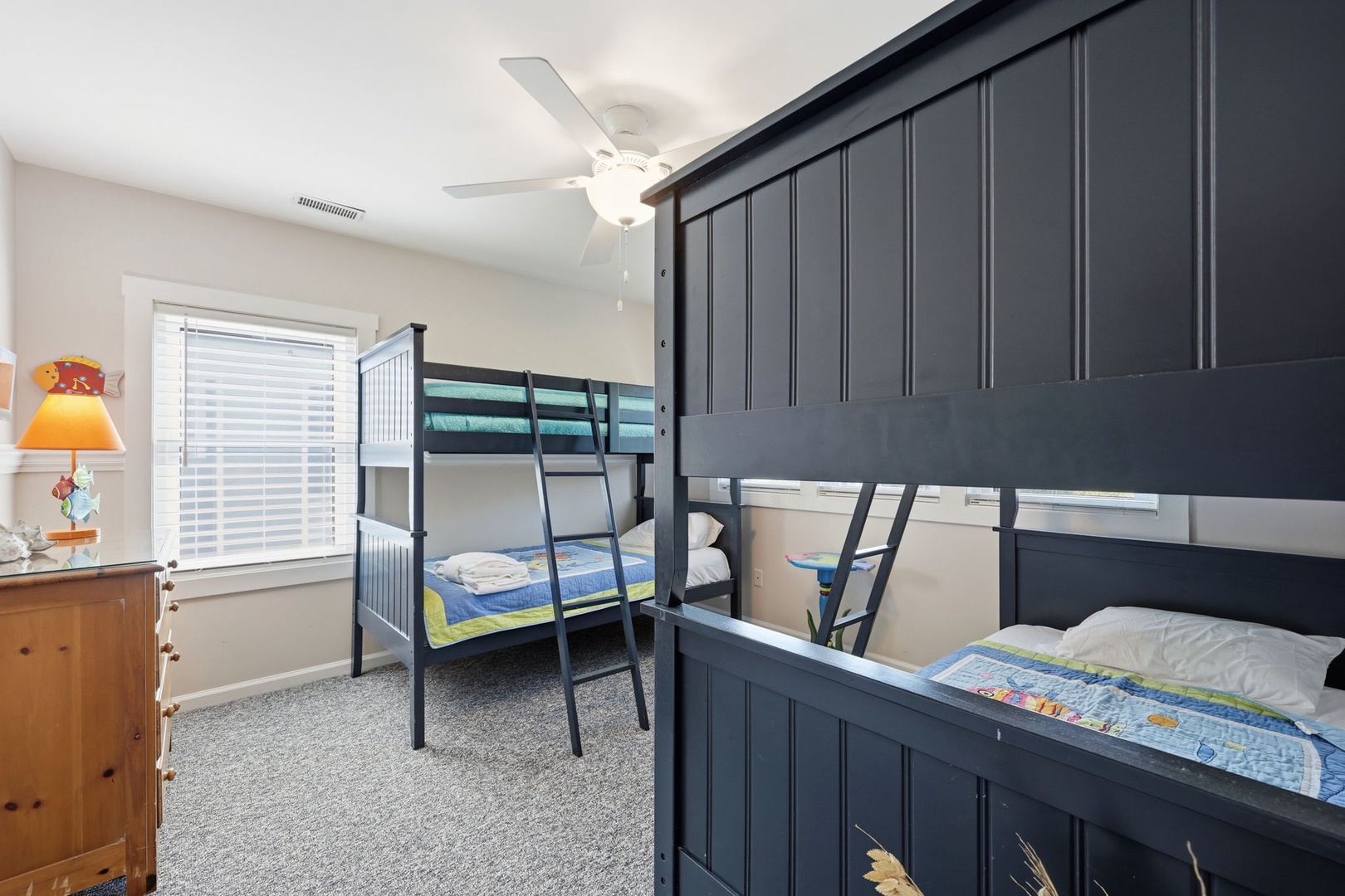 This cozy bunk room offers comfortable sleeping arrangements for the kids, featuring charming nautical-themed bedding, soft carpeting, and a ceiling fan to keep everyone cool during warm summer nights.