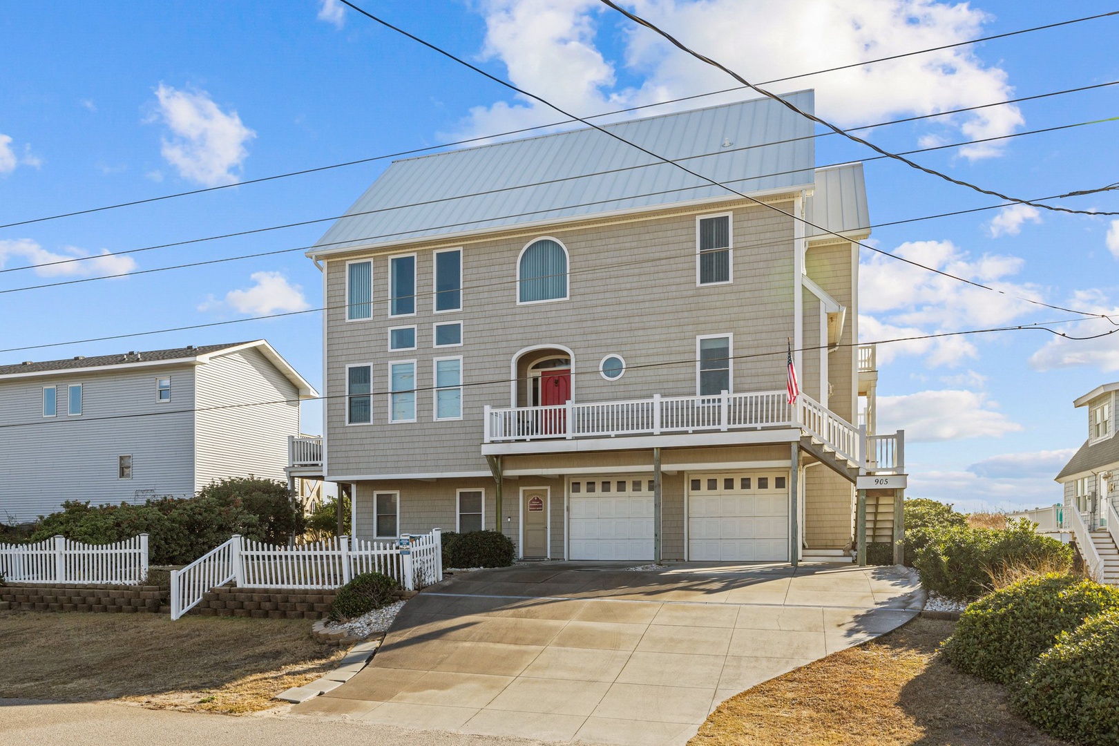 Two-story coastal vacation home with wraparound deck and garage, perfectly positioned in a quiet beachside neighborhood.