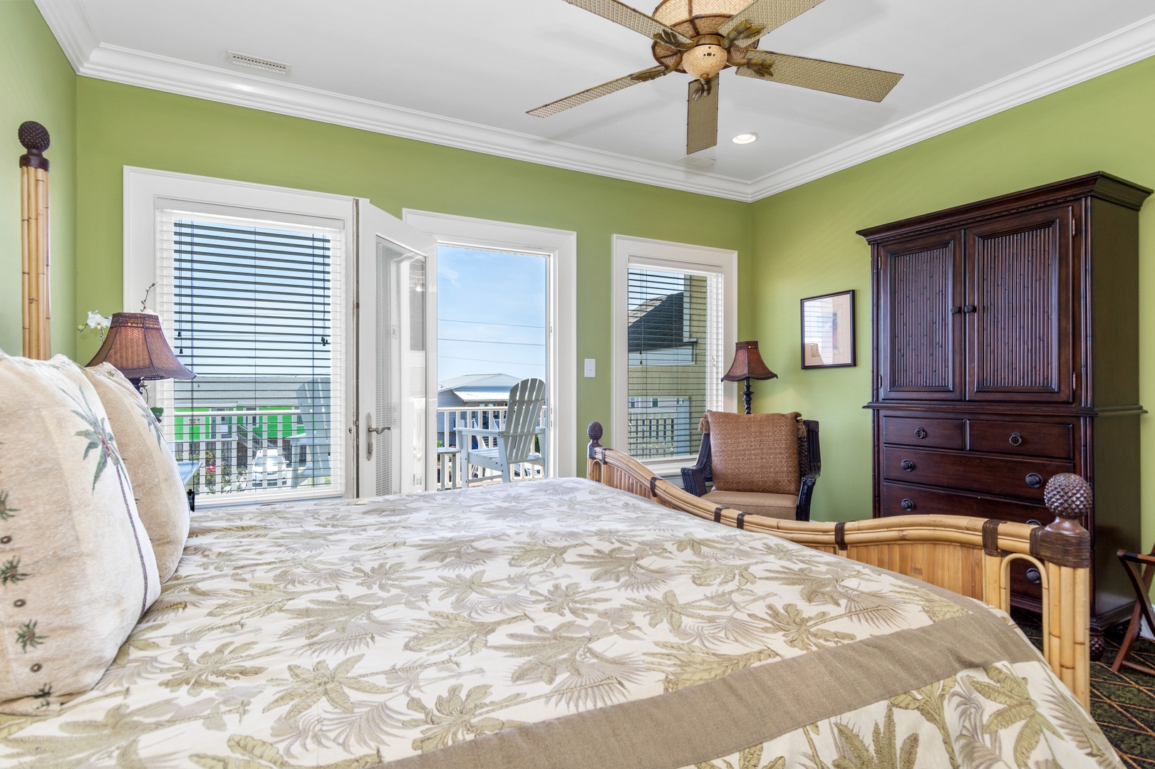 Wake up in this tranquil green bedroom where coastal breezes flow through French doors leading to your private balcony overlooking charming outdoor seating.