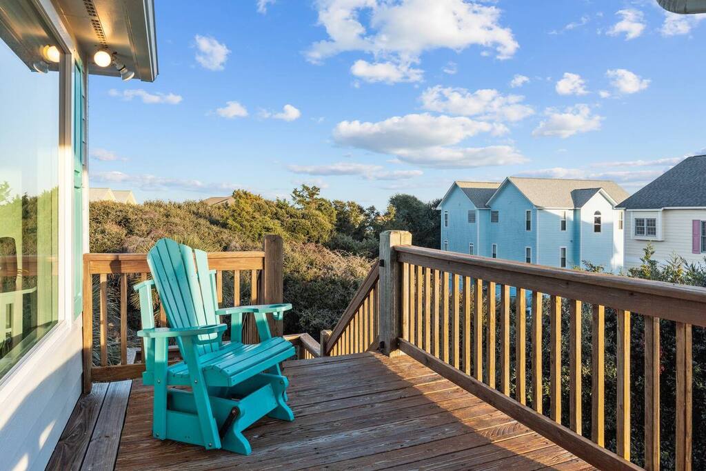 Relax on your private deck with turquoise Adirondack chairs, enjoying peaceful neighborhood views and coastal charm.
