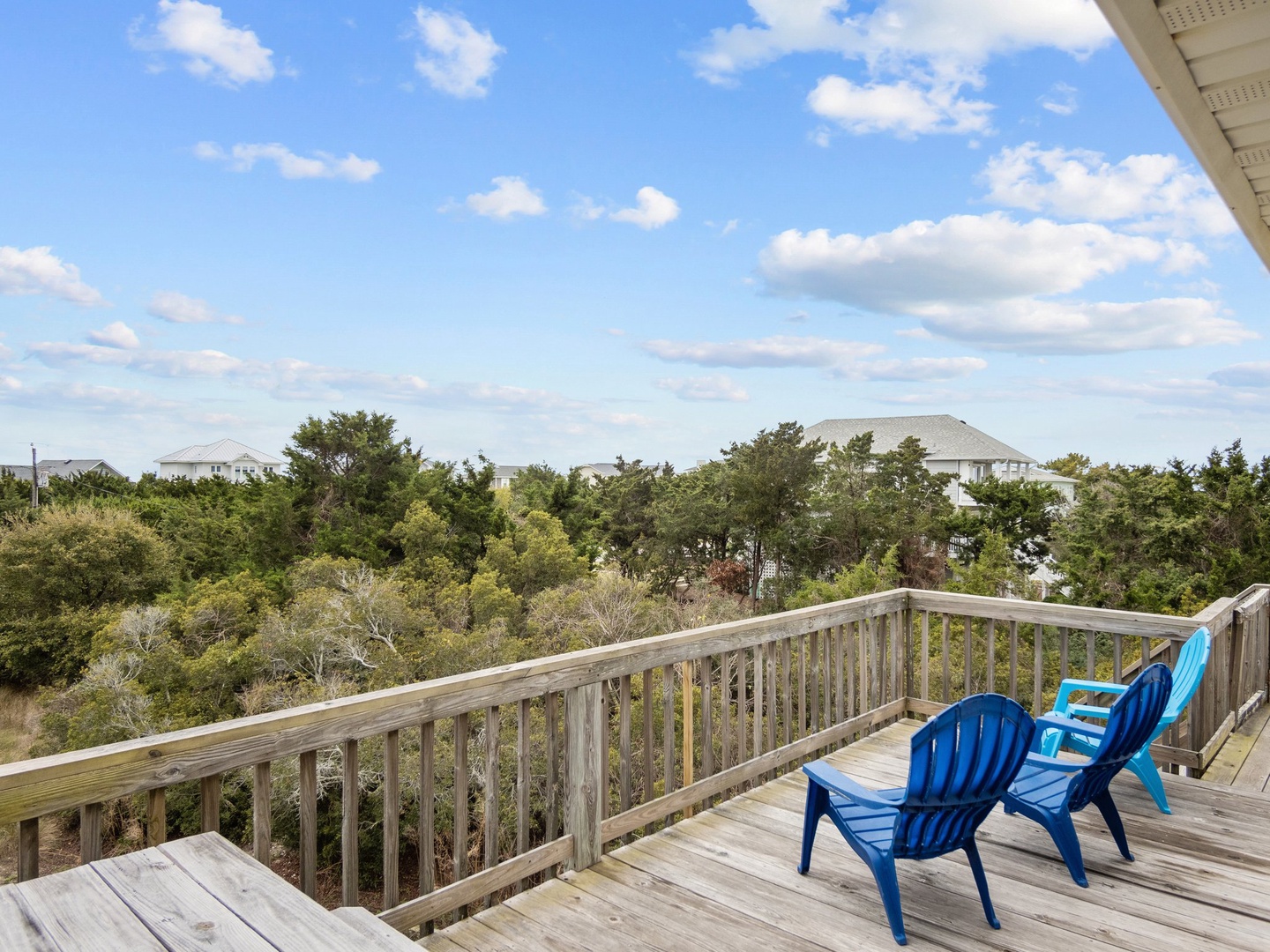 Expansive deck overlooks peaceful neighborhood treetops and distant homes under bright coastal sky.