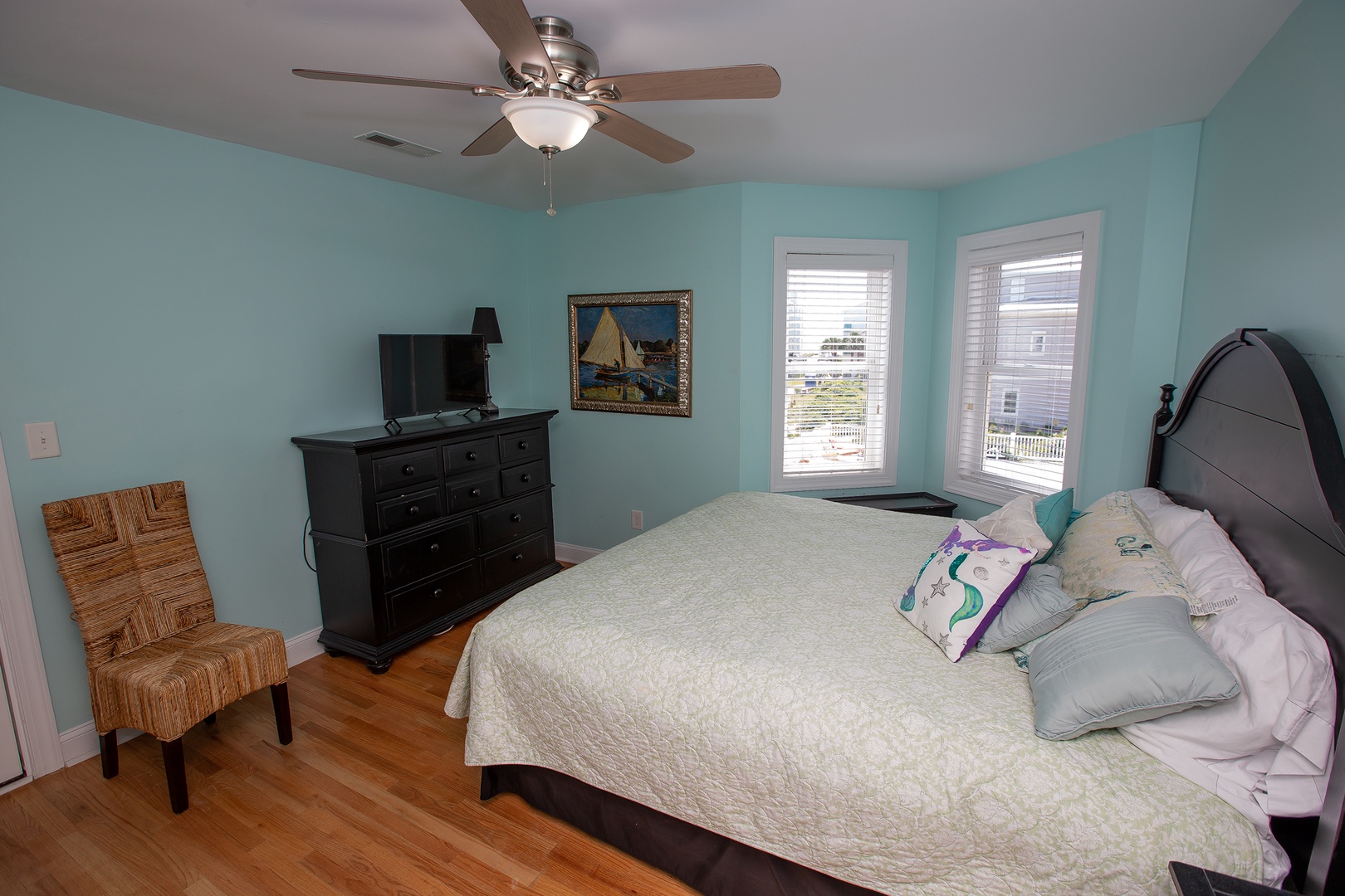 Drift into peaceful sleep in this airy bedroom with coastal charm, soft turquoise walls, and warm hardwood floors underfoot.