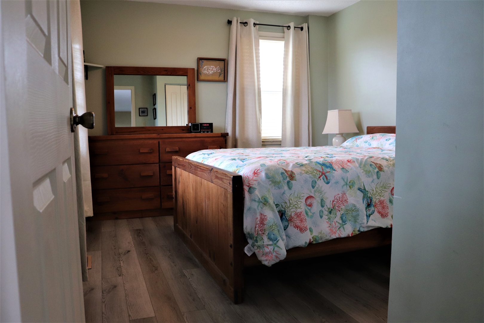 Settle into your peaceful bedroom featuring a comfortable queen bed, warm wood furnishings, and natural light streaming through soft curtains.