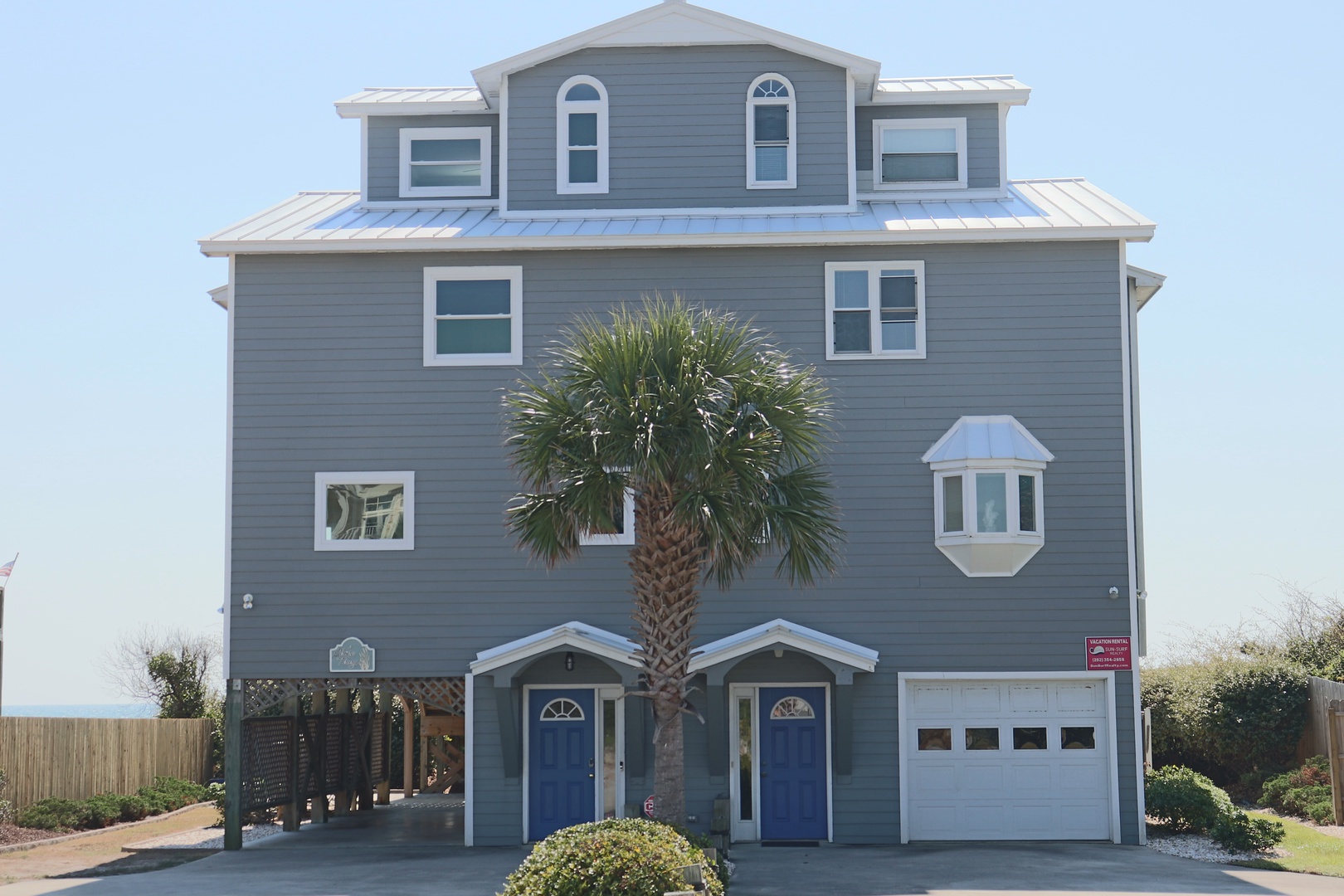 This impressive three-story coastal home features charming blue doors and a towering palm tree, creating the perfect beachside retreat.