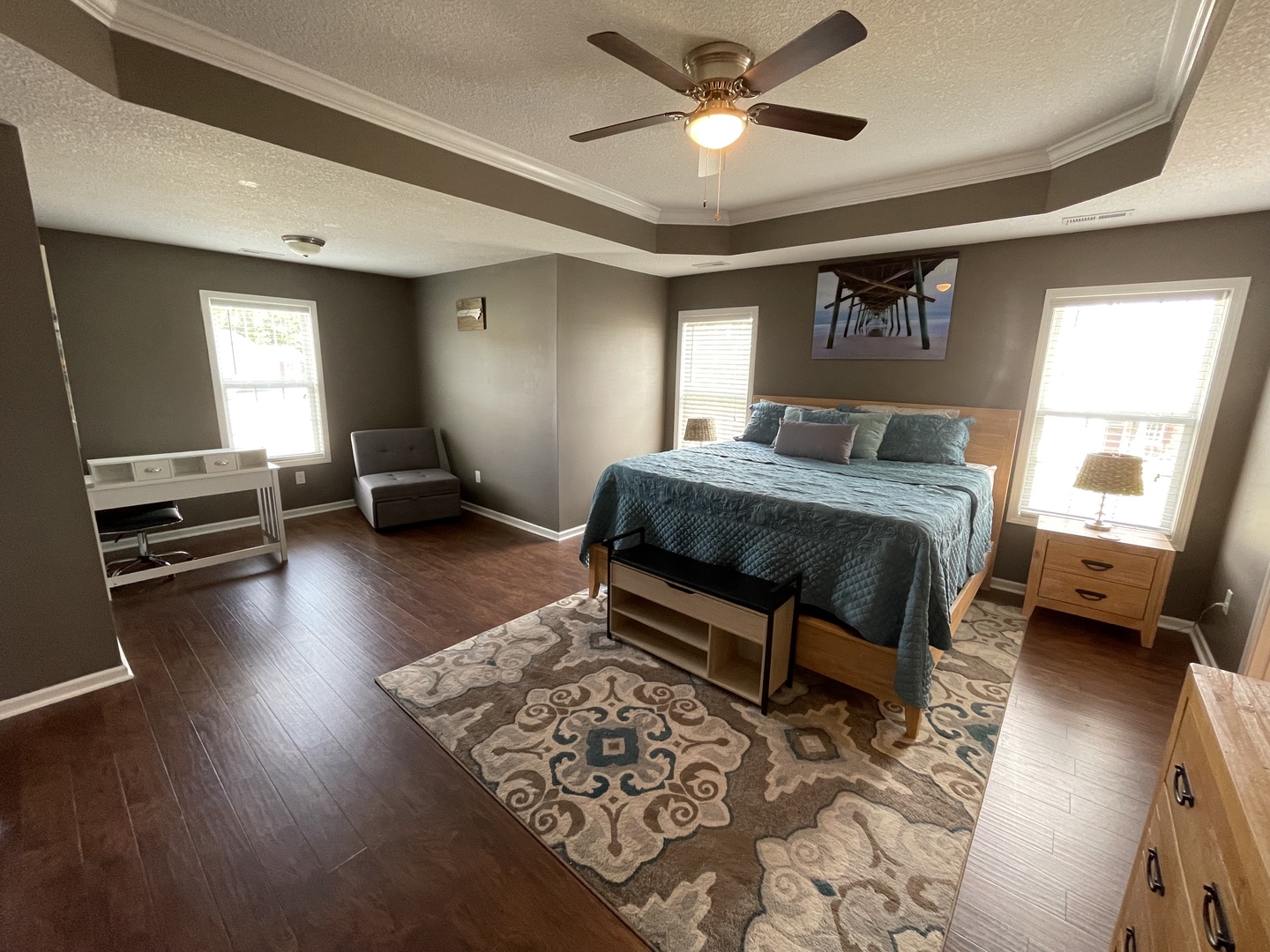 Relax in your spacious bedroom with dark wood floors, calming gray walls, and a ceiling fan for comfort.