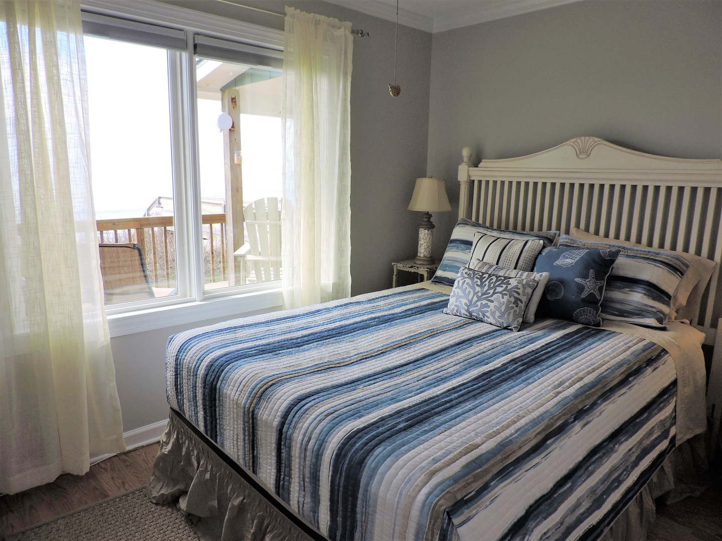 Your coastal bedroom sanctuary awaits with soft blue striped linens and gentle morning light streaming through balcony doors.