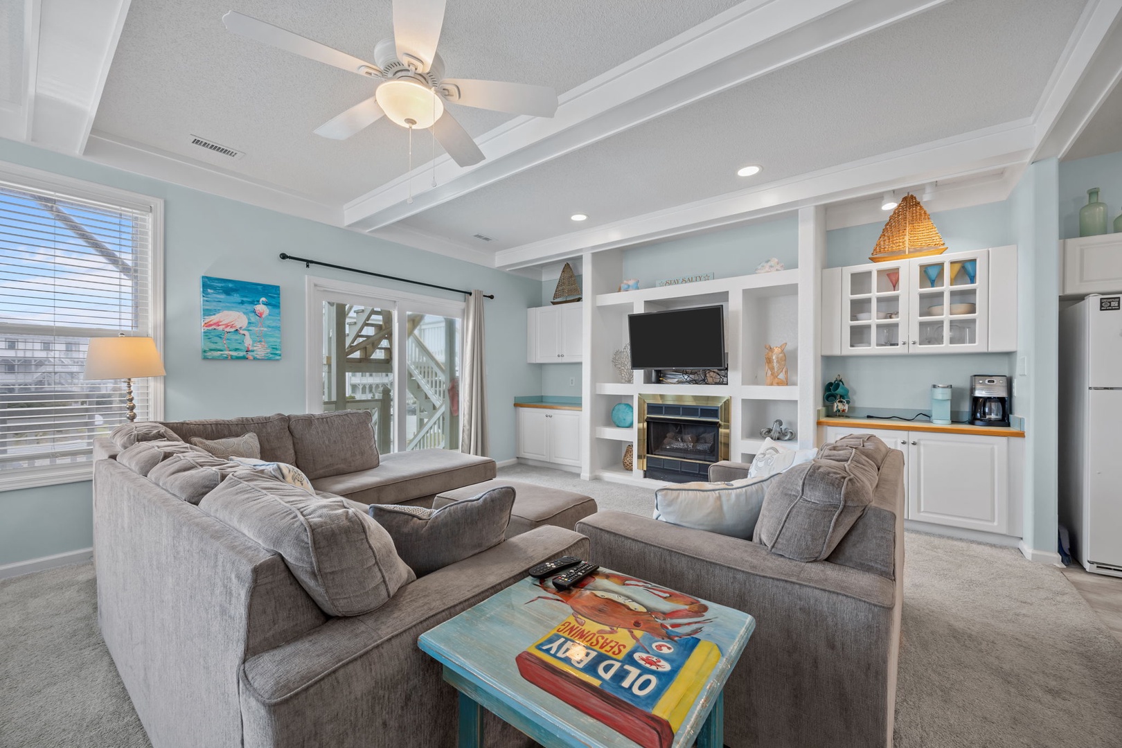 Sink into plush sectional seating in your bright, coastal-themed living space featuring built-in entertainment center and modern kitchen.