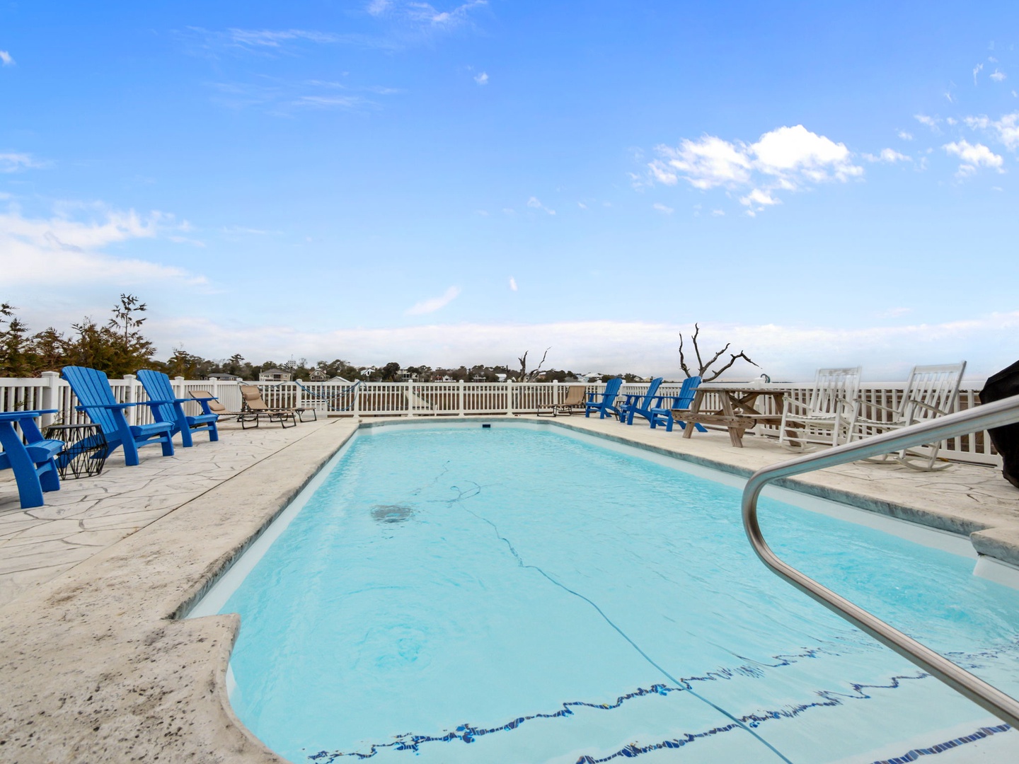 Relax poolside in vibrant blue chairs while soaking up coastal views from this elevated deck oasis.