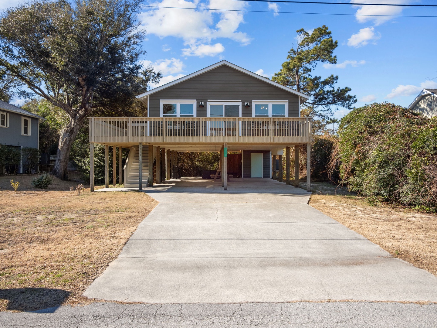 Elevated beach house with wraparound deck overlooking mature trees and peaceful neighborhood setting.