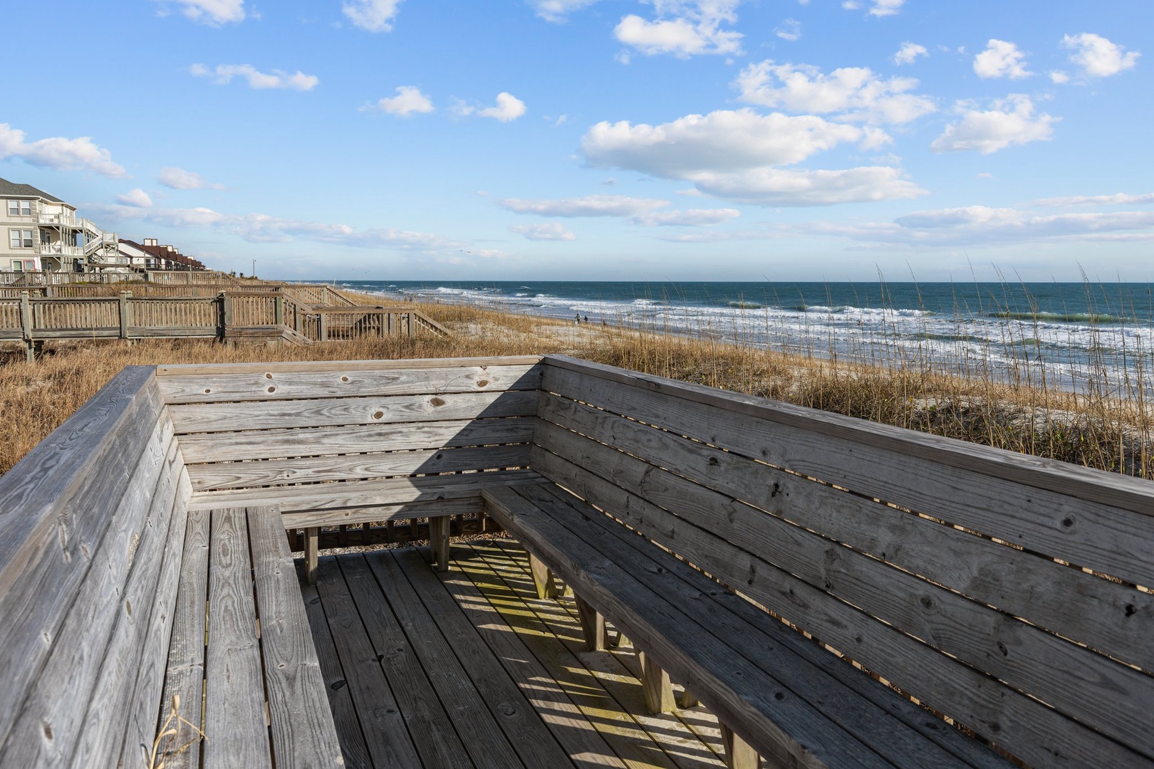 Wooden boardwalk leads to pristine beachfront with ocean waves and coastal homes nearby.