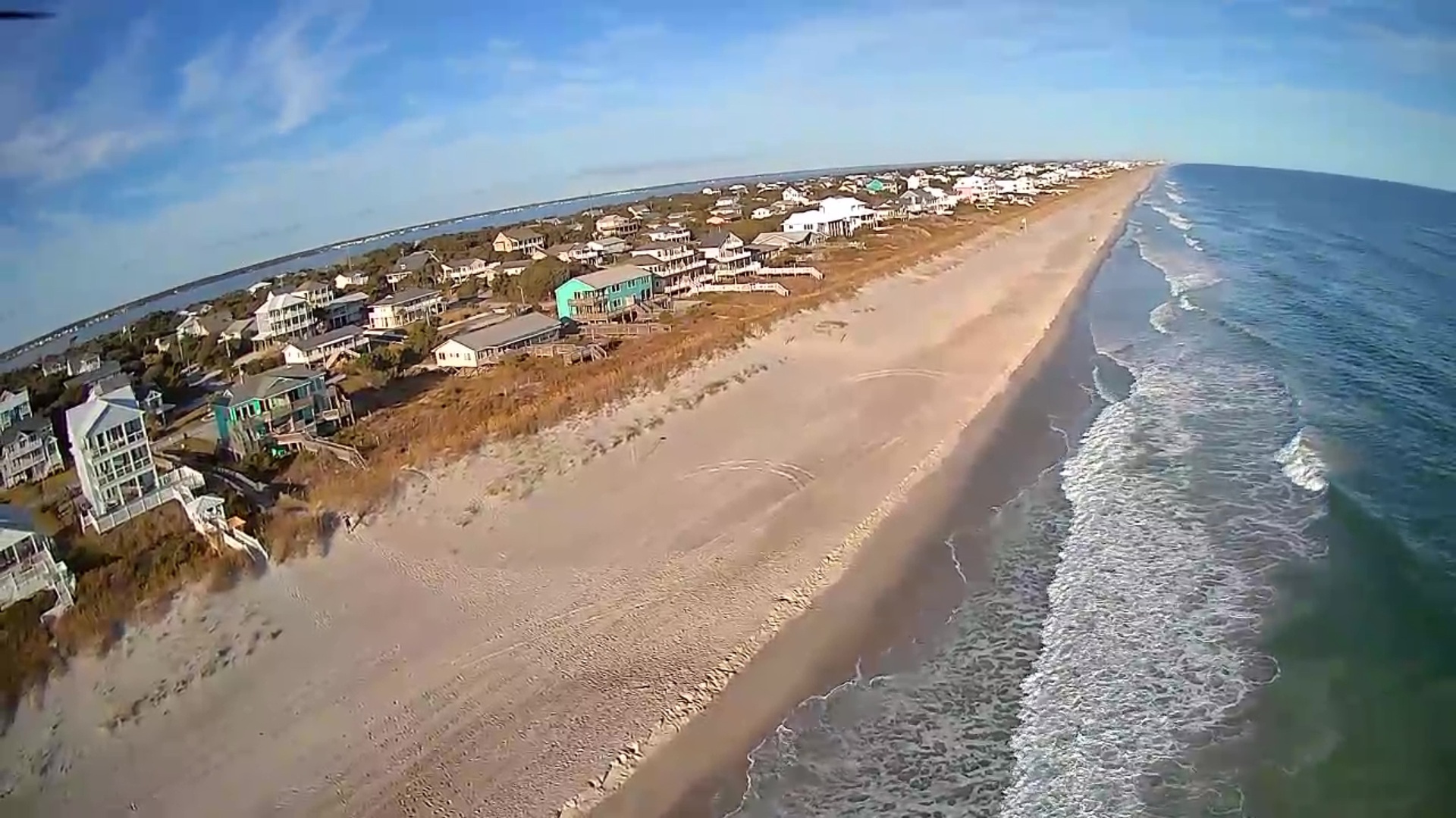 Stunning aerial view of pristine coastline with expansive sandy beach and oceanfront vacation homes along the shore.