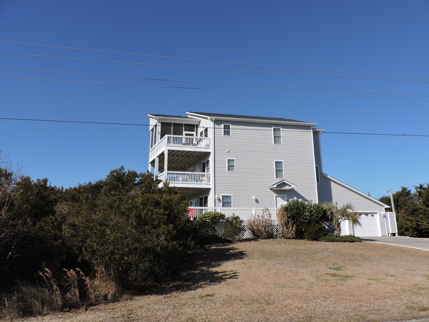 Multi-level beachside retreat with spacious balconies nestled among coastal vegetation under brilliant blue skies.